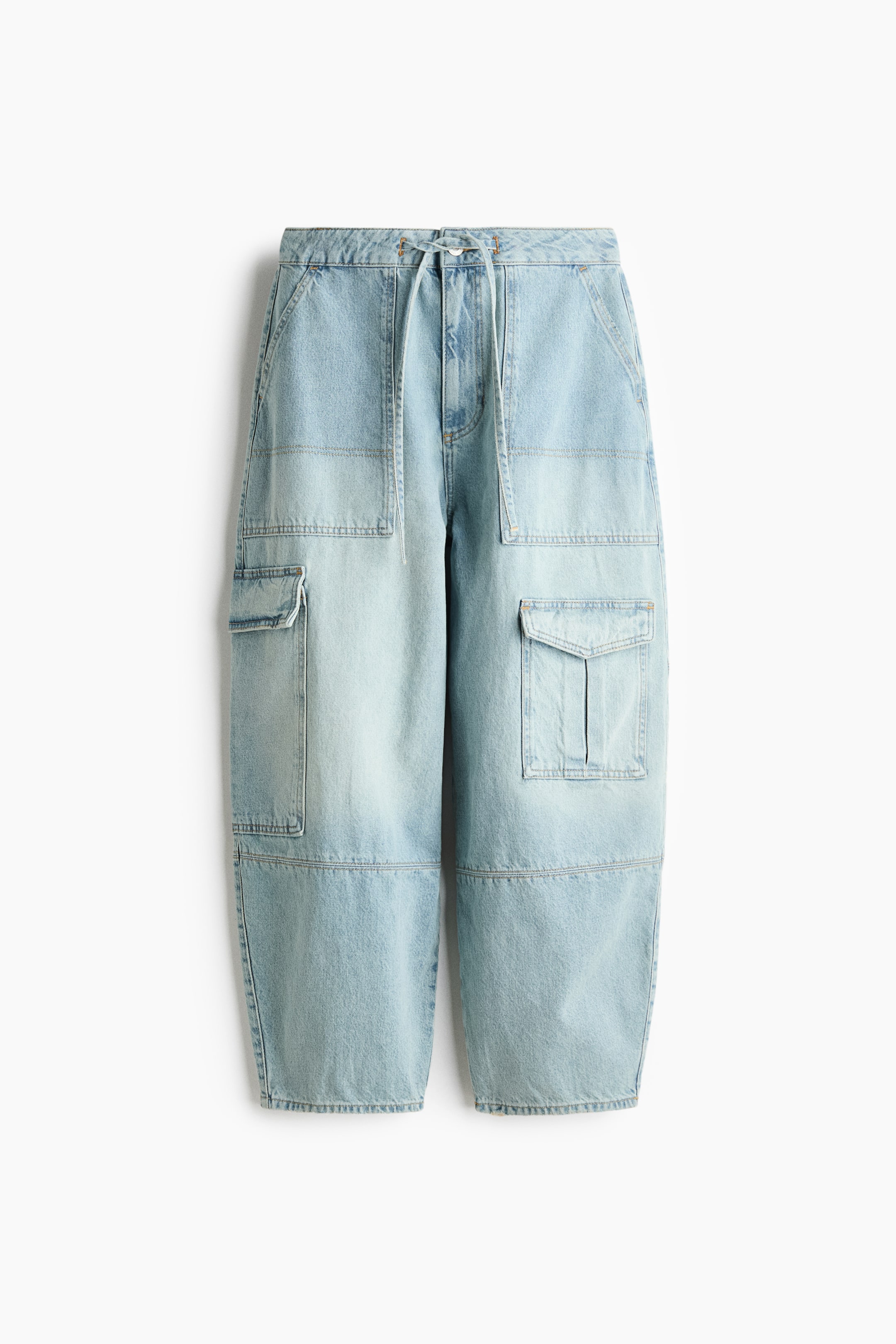 Vis større bilde: De lyseblå denim cargobuksene er vendt mot fronten, med et snorbelte med synlige knytebånd, skrålommer på sidene og store cargolommer med klaffelukking på lårene. Buksene har også en panelkonstruksjon med synlige sømmer og en avslappet, vid passform med ferdige falder.