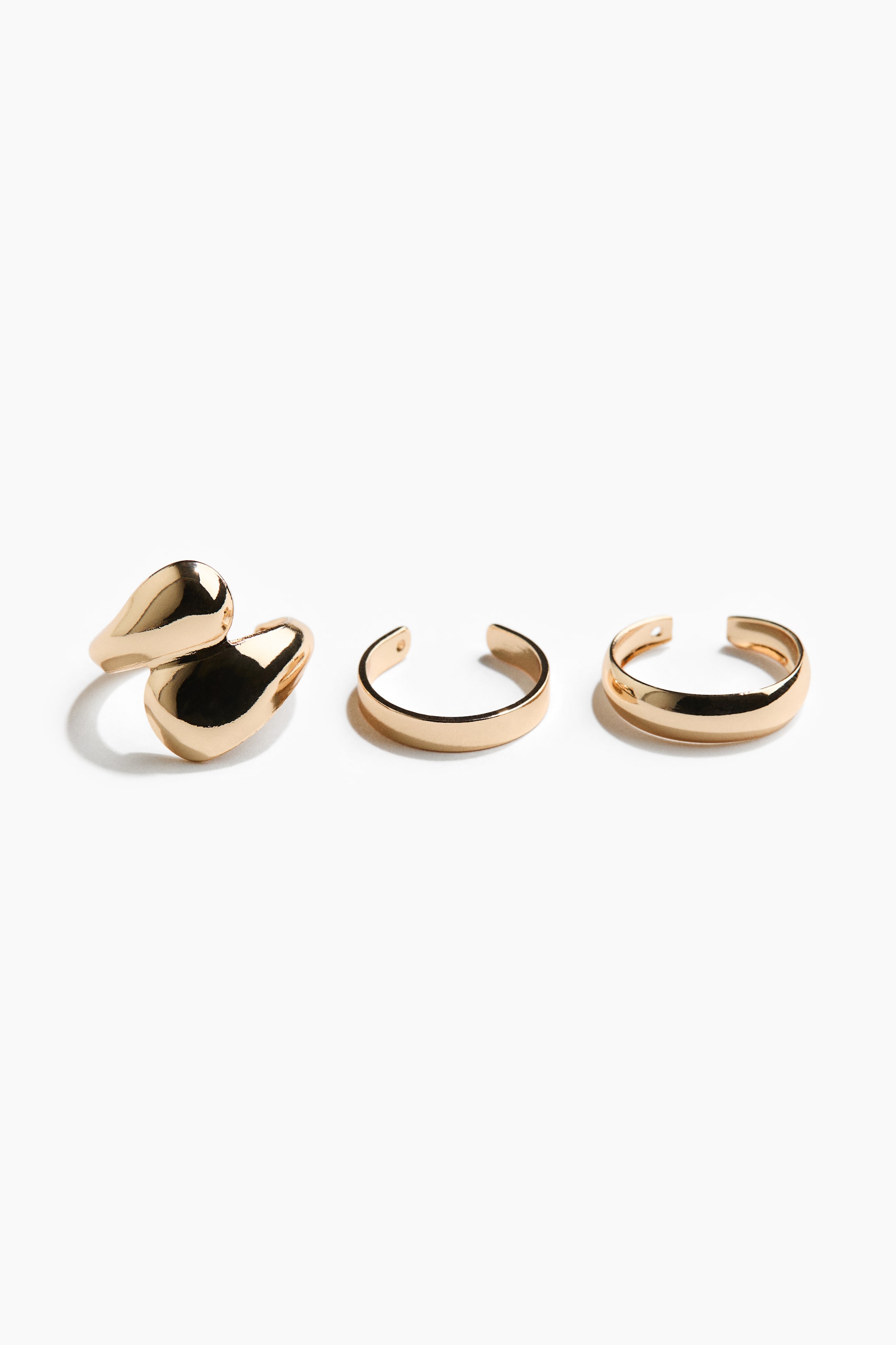 Agrandir l'image: Un ensemble de trois manchettes d'oreille dorées présente des designs distincts. Une manchette arbore une forme sculpturale et fluide avec deux sections arrondies connectées, tandis que les deux autres manchettes présentent des bandes lisses et ouvertes avec leurs ouvertures orientées vers l'avant.