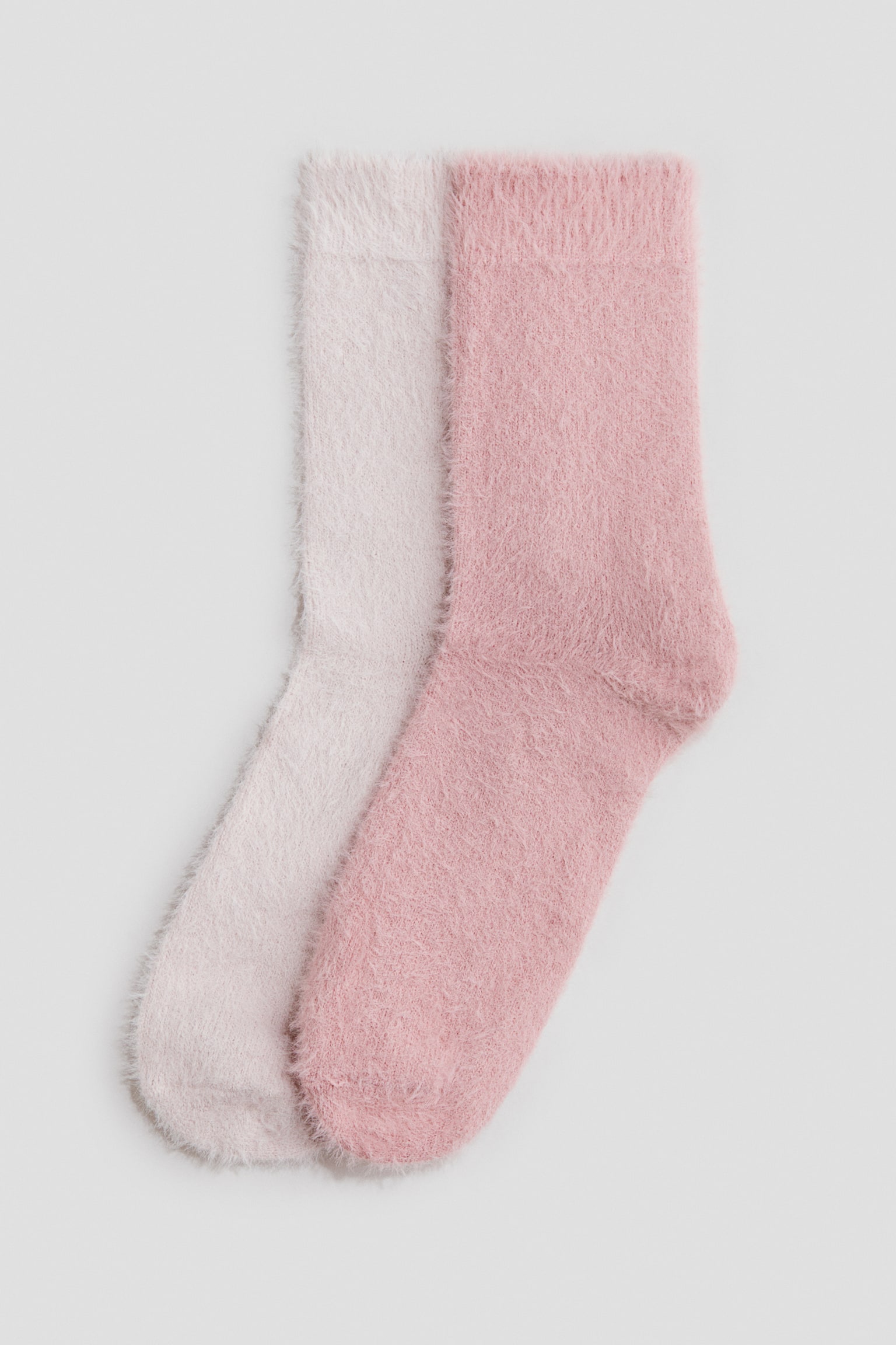 Two fuzzy knitted socks are laid flat in an overlapping arrangement, with a dusty rose pink sock resting on top of a pale blush pink sock. Both socks display a soft, fluffy texture and feature ribbed cuffs at the top.