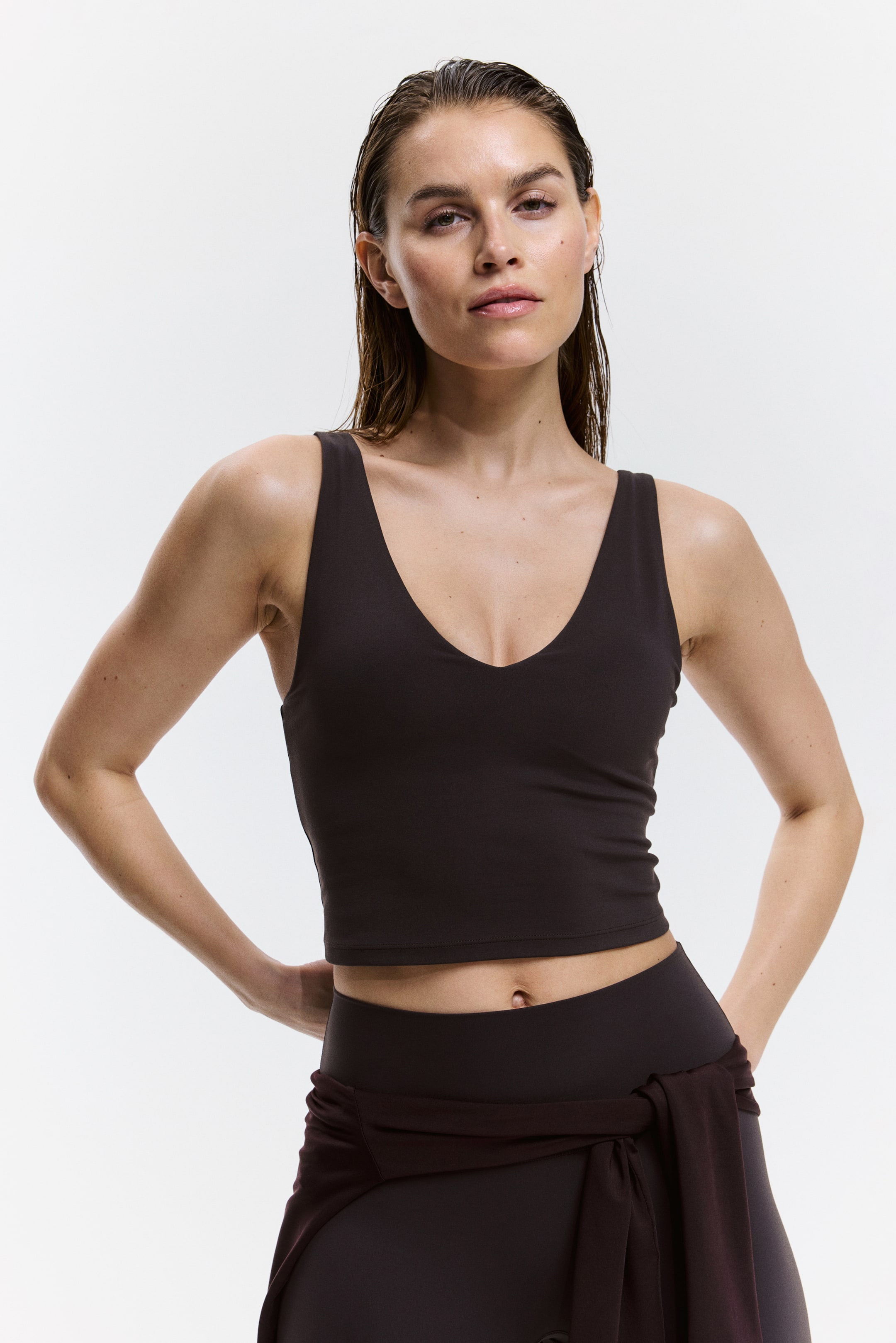 View larger image: A dark brown crop top featuring a deep V-neck and wide shoulder straps, offering a snug fit and ending at the midriff.