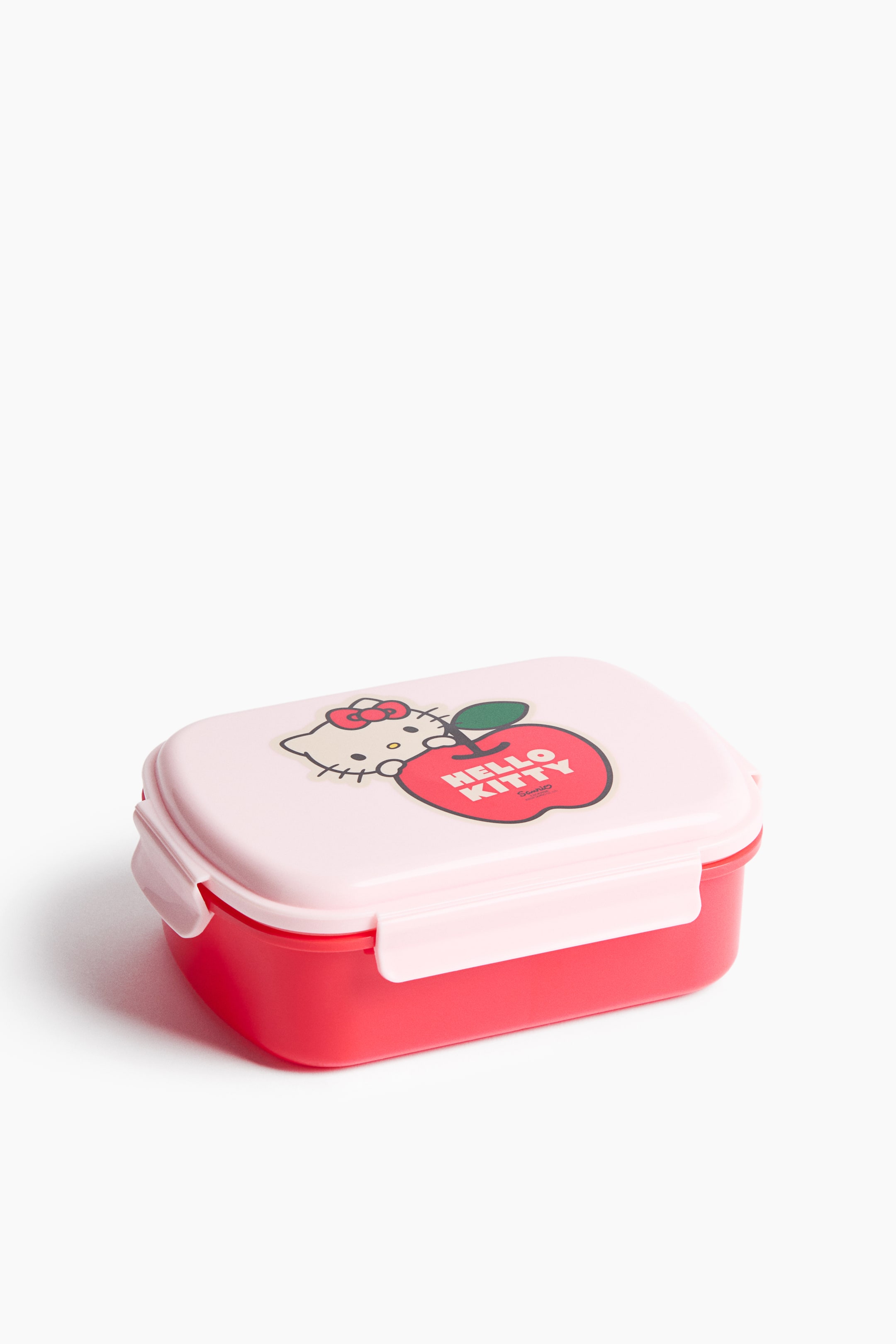 View larger image: This rectangular lunchbox showcases a red base paired with a light pink lid. The lid highlights a graphic of the Hello Kitty character beside a red apple, accompanied by the text "HELLO KITTY." Two light pink clips secure the lid on the sides.