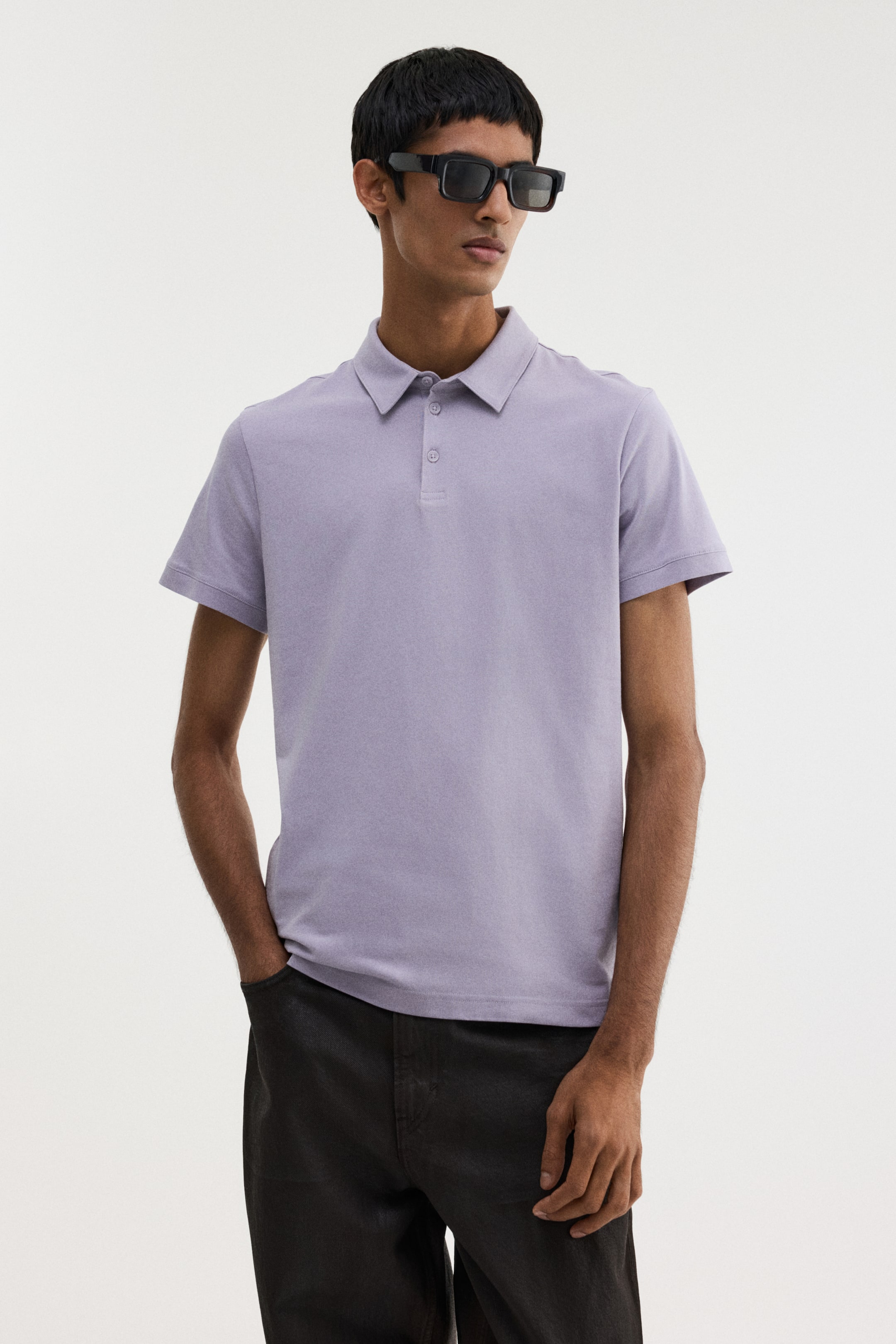 View larger image: A light purple polo shirt is being presented on a model, seen from a slight front-right angle. It is featuring a flat polo collar, a two-button placket with tone-on-tone buttons, and short sleeves. The shirt is displaying a smooth fit across the torso.