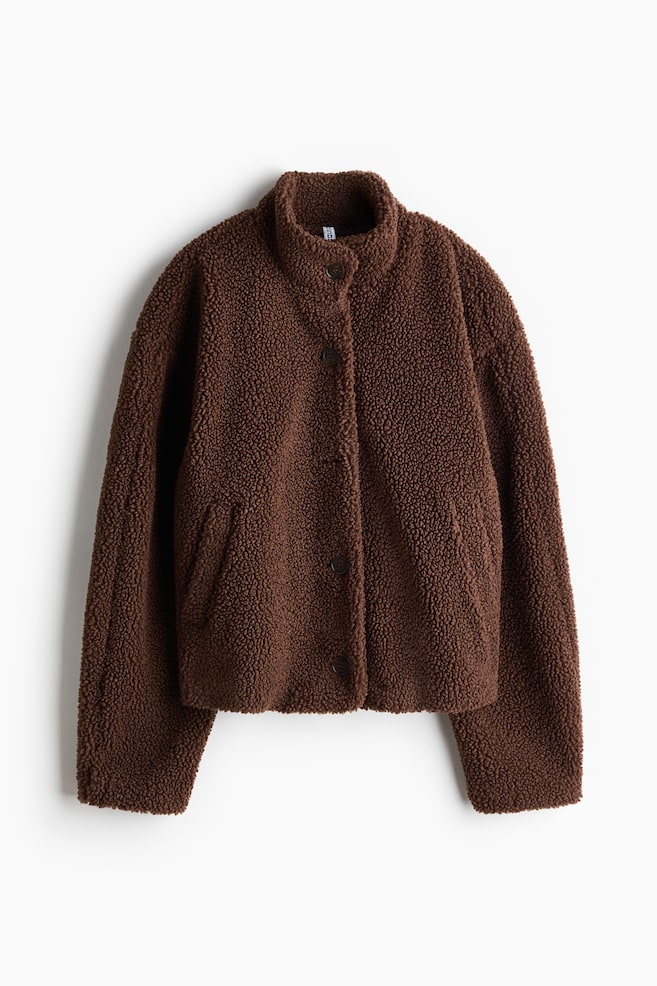 A brown teddy fleece jacket is facing front, featuring a textured pile fabric, a stand-up collar, and a front button closure. The jacket is displaying long, relaxed sleeves and two side welt pockets. - 1