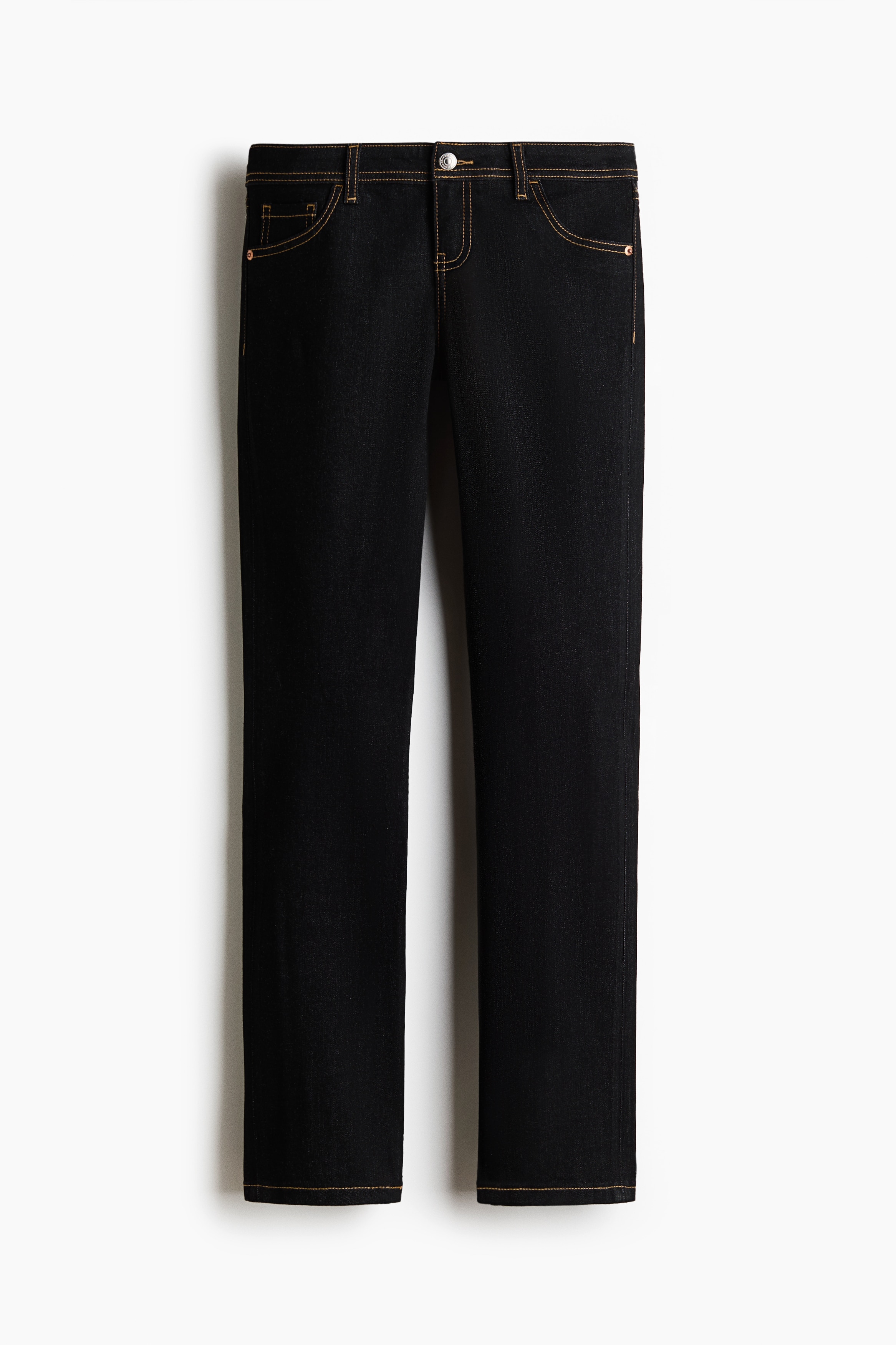 MÃ¶rktvÃ¤ttade jeans i denim med extra lÃ¥g midja, kontrastsÃ¶mmar och slim fit bÃ¤rs av modellen. Jeansen stylas med en kort cremefÃ¤rgad T-shirt, en Ã¶ppen ljus jacka och vita sneakers.
