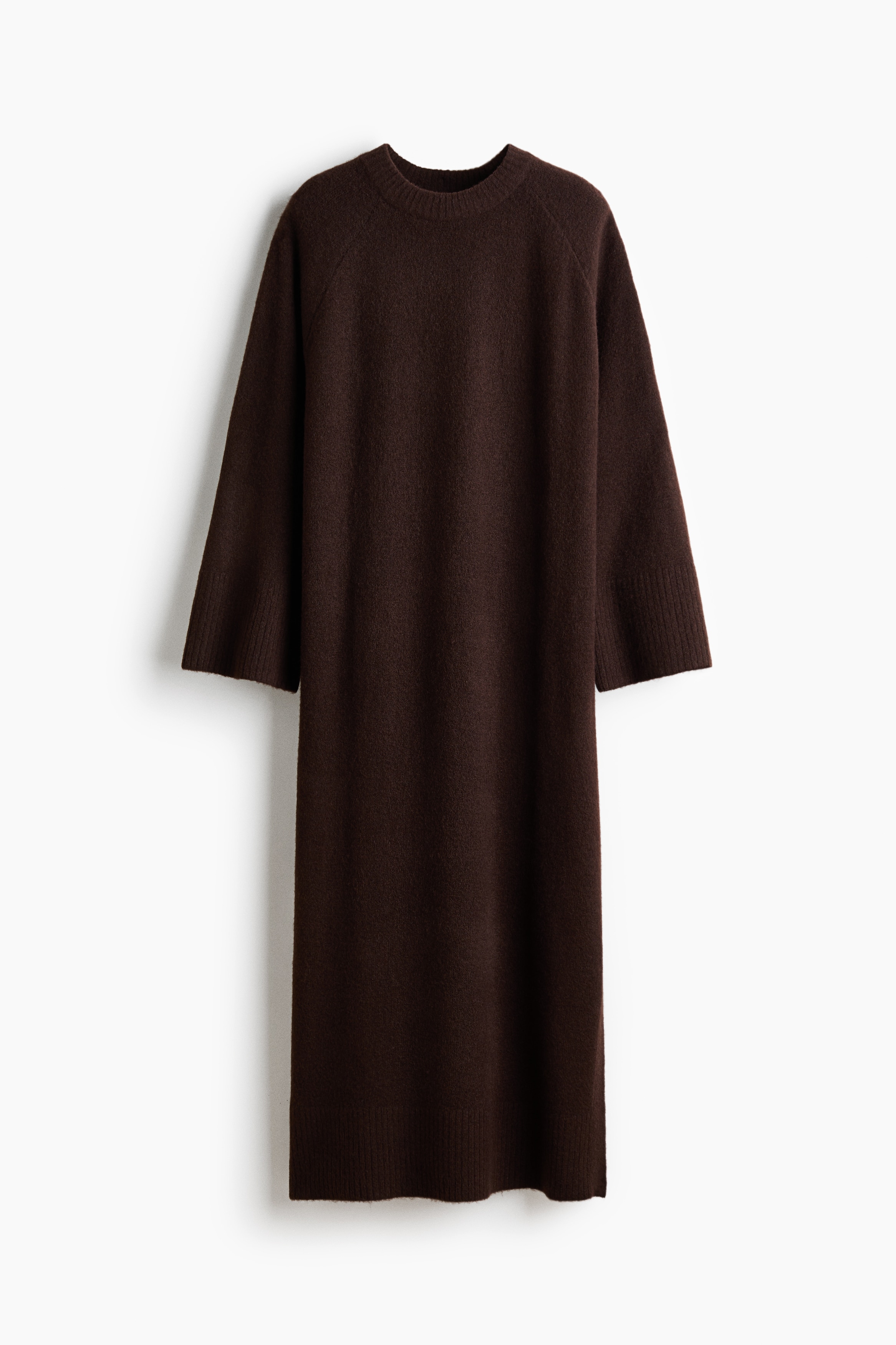 Ein dunkelbraunes Strick-Maxikleid wird von dem Model getragen, wÃ¤hrend es sitzt und das Kinn auf einer Hand abstÃ¼tzt. Das Kleid verfÃ¼gt Ã¼ber einen runden, gerippt eingefassten Ausschnitt, lange Ãrmel mit breiten RippbÃ¼ndchen und eine weiche, strukturierte OberflÃ¤che.