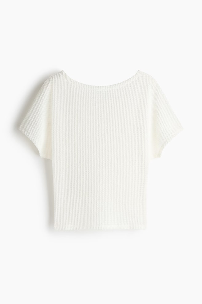 A white waffle knit top is featuring a wide boat neckline, short, relaxed sleeves, and a straight hem. - 1