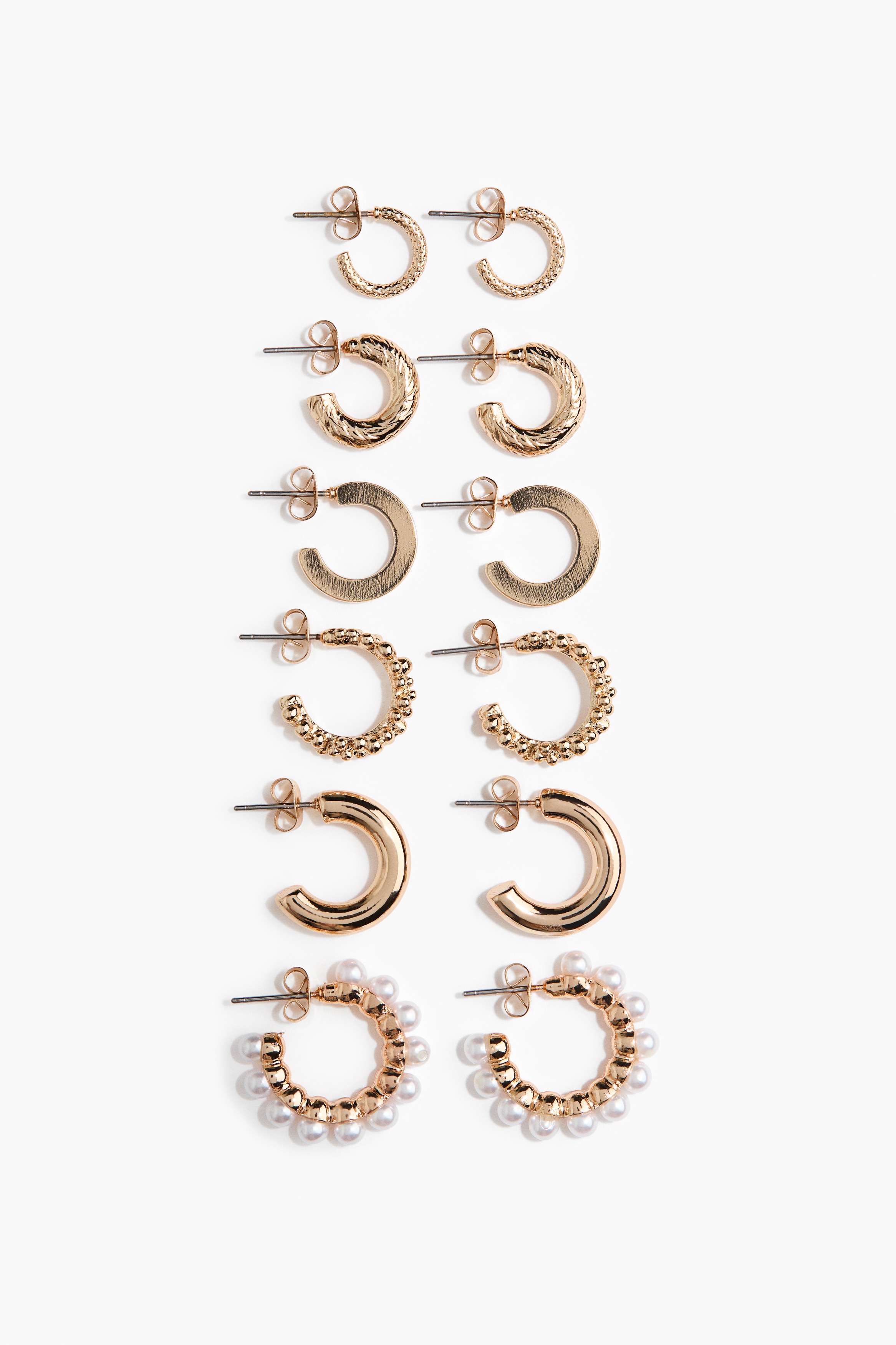 Small, textured metal hoop earrings with a beaded design are being worn by the model. The earrings are styled with a high, ruffled collar and a cream-coloured textured cape.