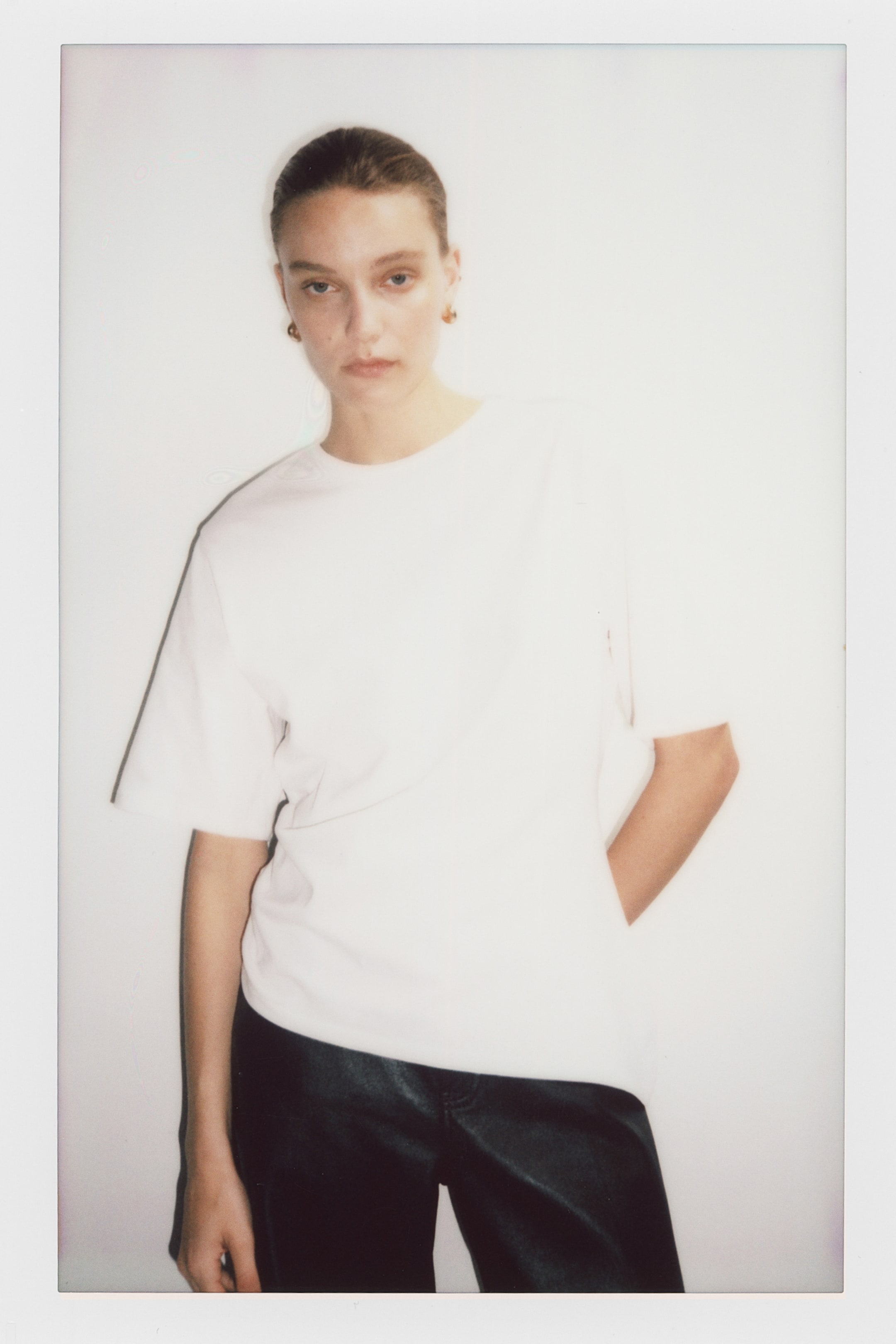 View larger image: A white t-shirt is showcased from a slight angle, featuring a round neckline, dropped shoulders, and short, relaxed-fit sleeves.