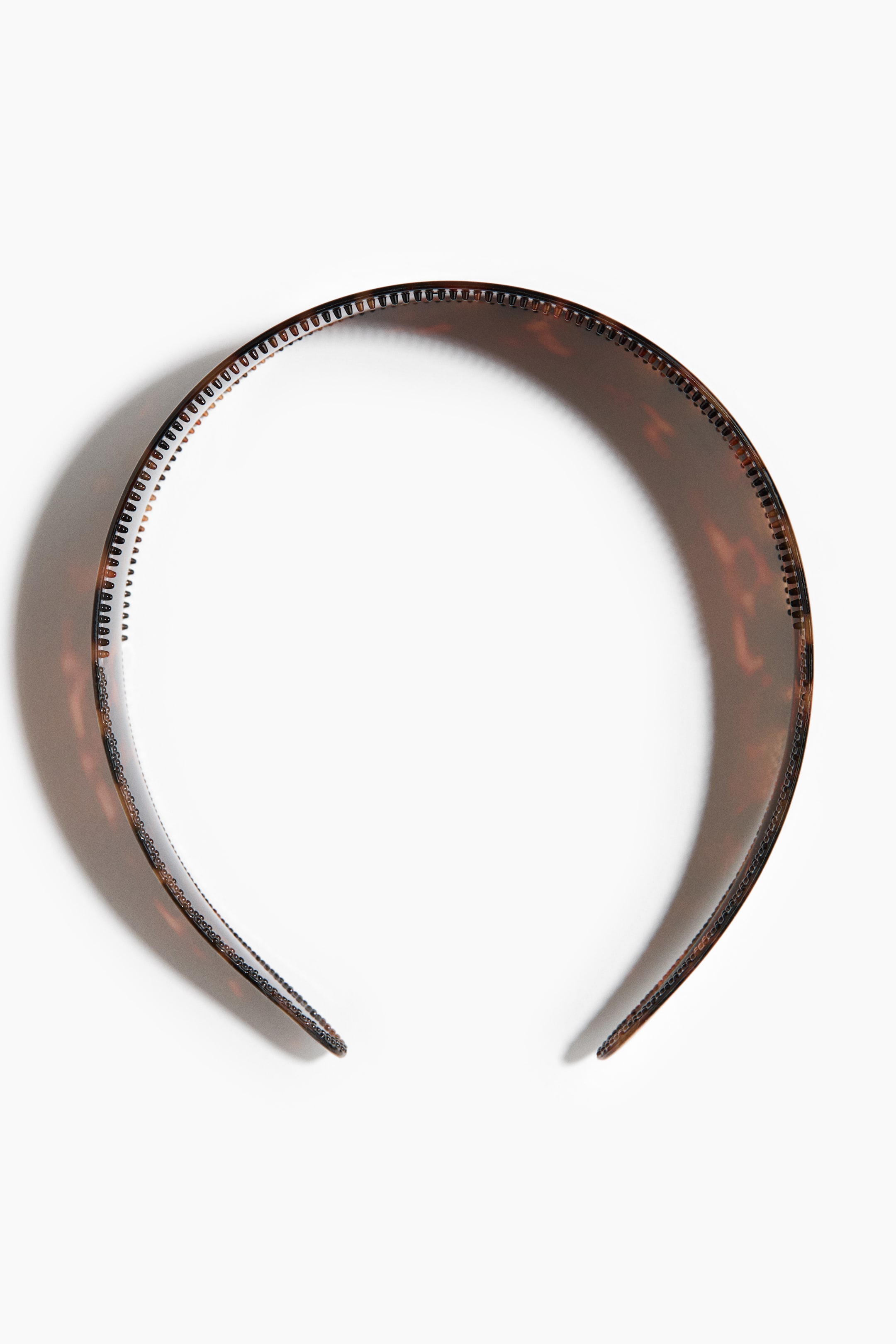 View larger image: A tortoiseshell headband is curved into a semi-circle. It features a brown and amber pattern, and small teeth line its inner edge.