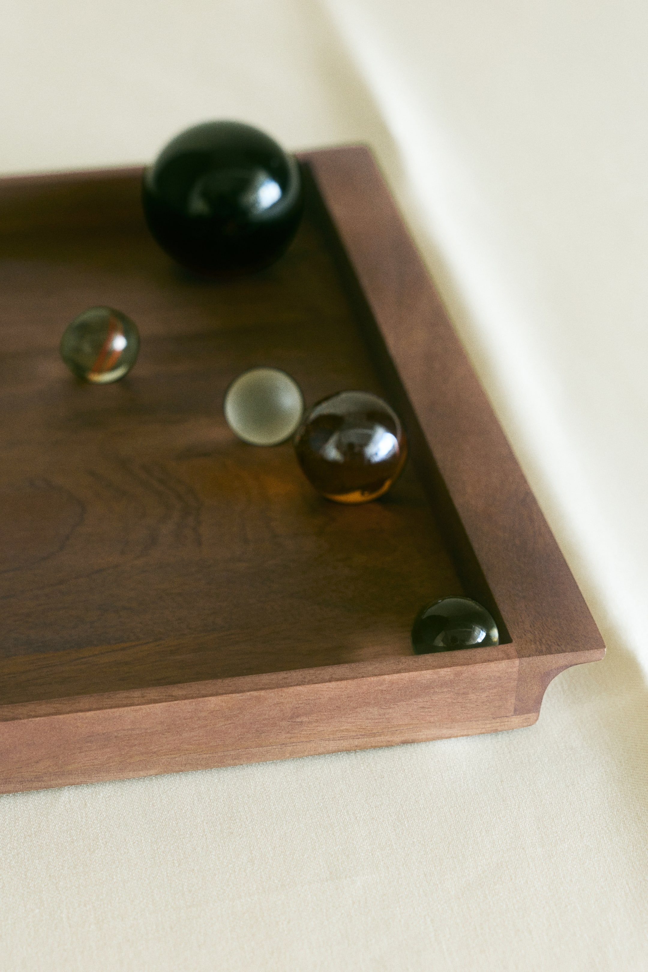 View larger image: A rectangular mango wood serving tray features a raised rim and natural dark brown wood grain in a close-up, high-angle view. Several decorative glass spheres of varying sizes and colours rest on the flat surface of the tray.