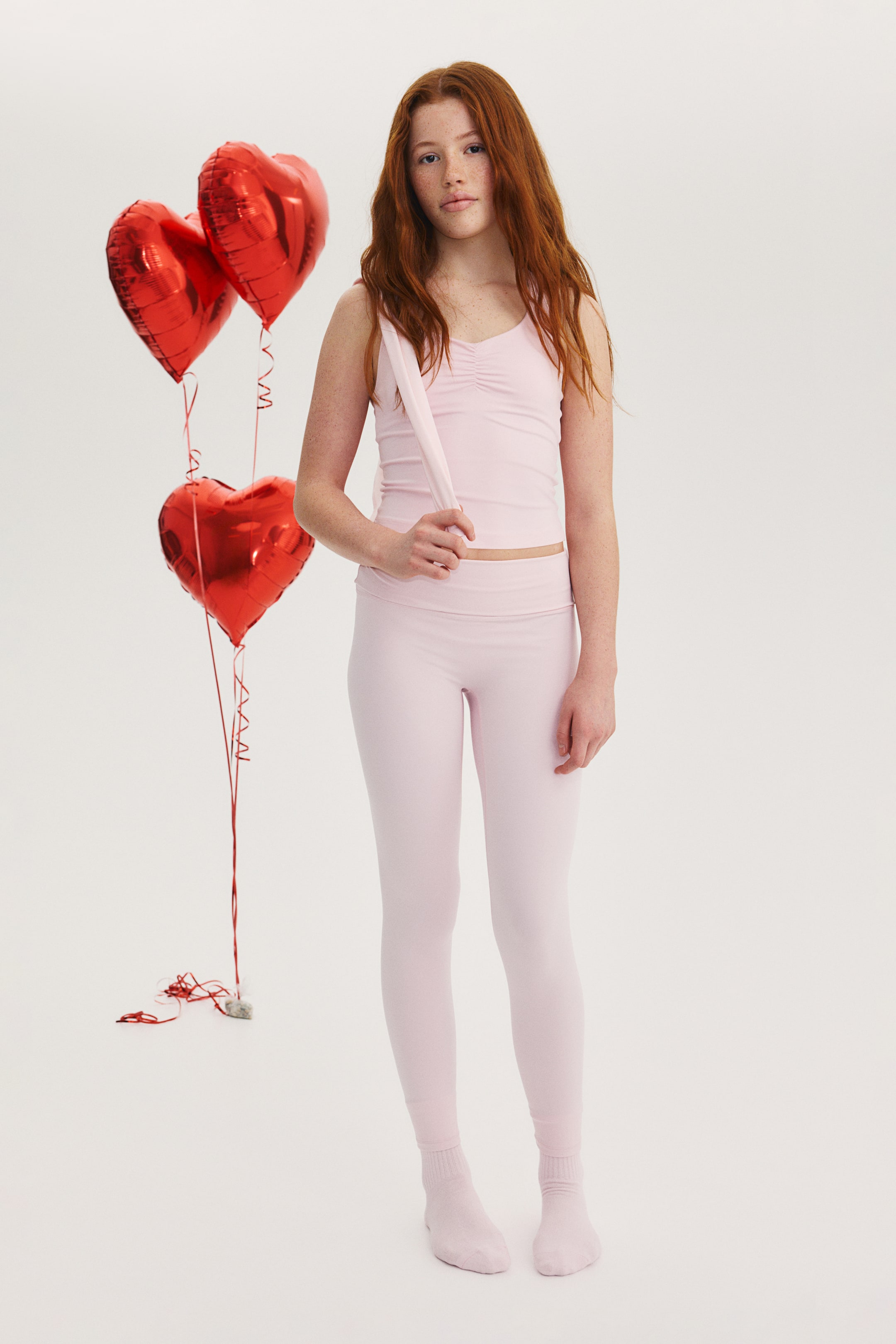 Visa större bild: Setet består av ett ljusrosa linne och matchande högmidjade leggings och visas framifrån. Linnet har V-ringning med rynkad detalj vid bysten och tunna axelband, där ett av axelbanden hänger ned över armen, och leggingsen i full längd har en bred linning.