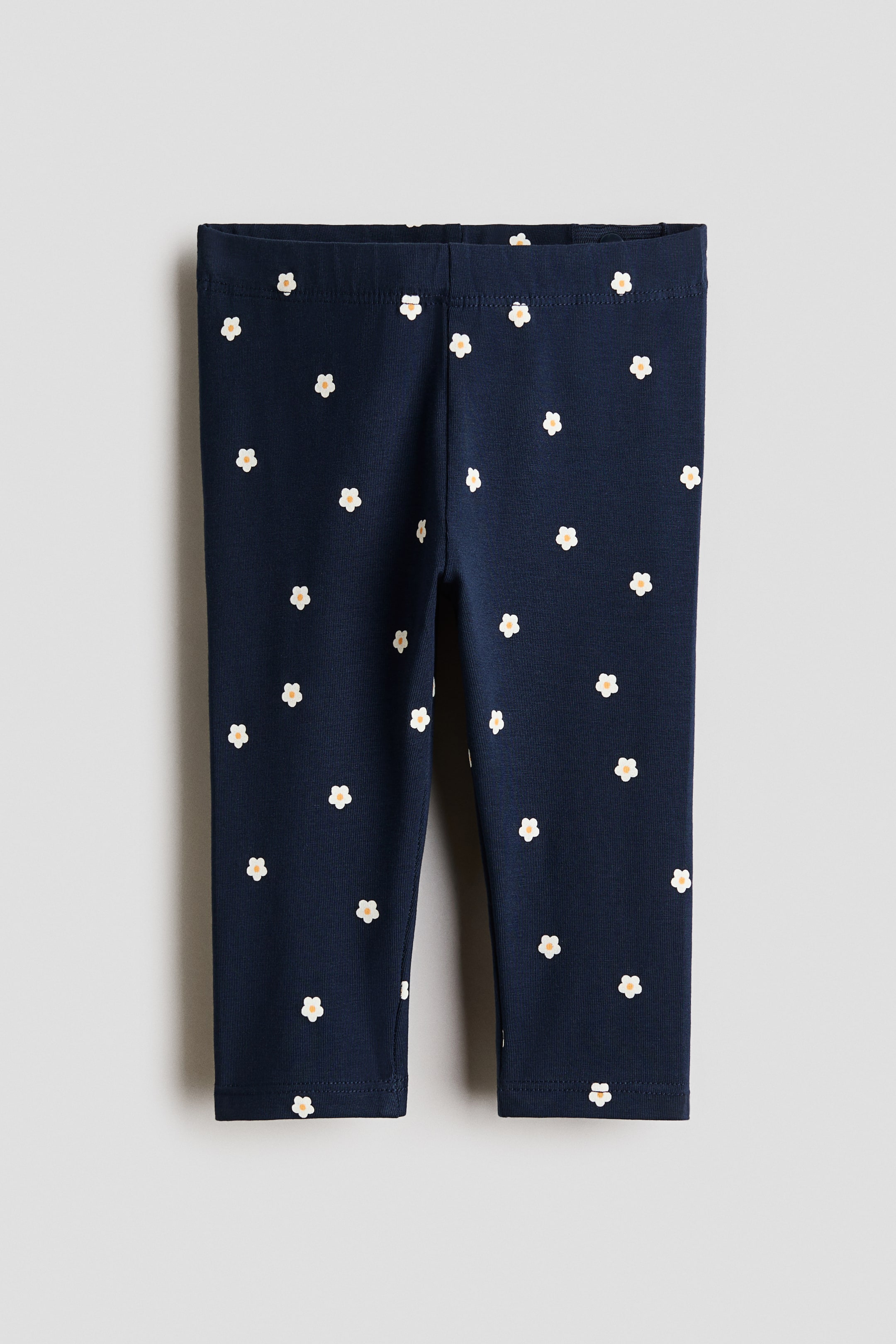 Visa större bild: Leggings visas framifrån och presenterar ett mörkblått jerseymaterial som är mönstrat med utspridda små vita blommor, var och en med en ljusgul mitt. En elastisk midjeband kompletterar designen.