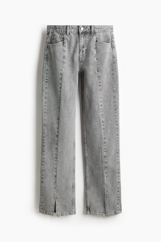 Vue de face d'une paire de jeans gris délavé, avec une fermeture à bouton, une braguette zippée et des coutures verticales surpiquées proéminentes courant le long du centre avant de chaque jambe. Les jeans sont finis avec de petites fentes aux ourlets extérieurs des chevilles. - 1