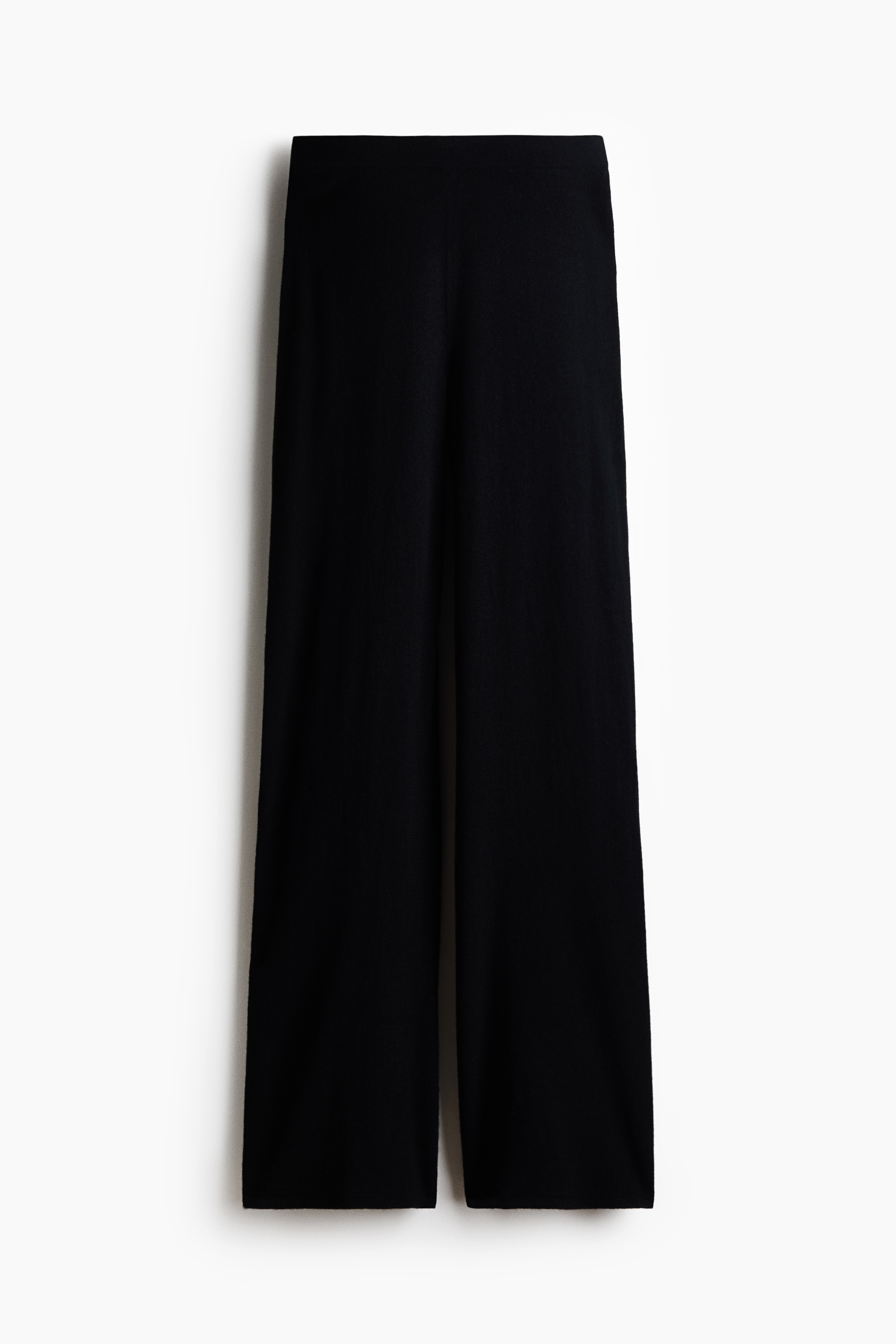 Soft knit trousers with a straight-leg cut are being worn by the model, who is seated with one knee raised. The trousers are styled with a matching long-sleeved knit top.