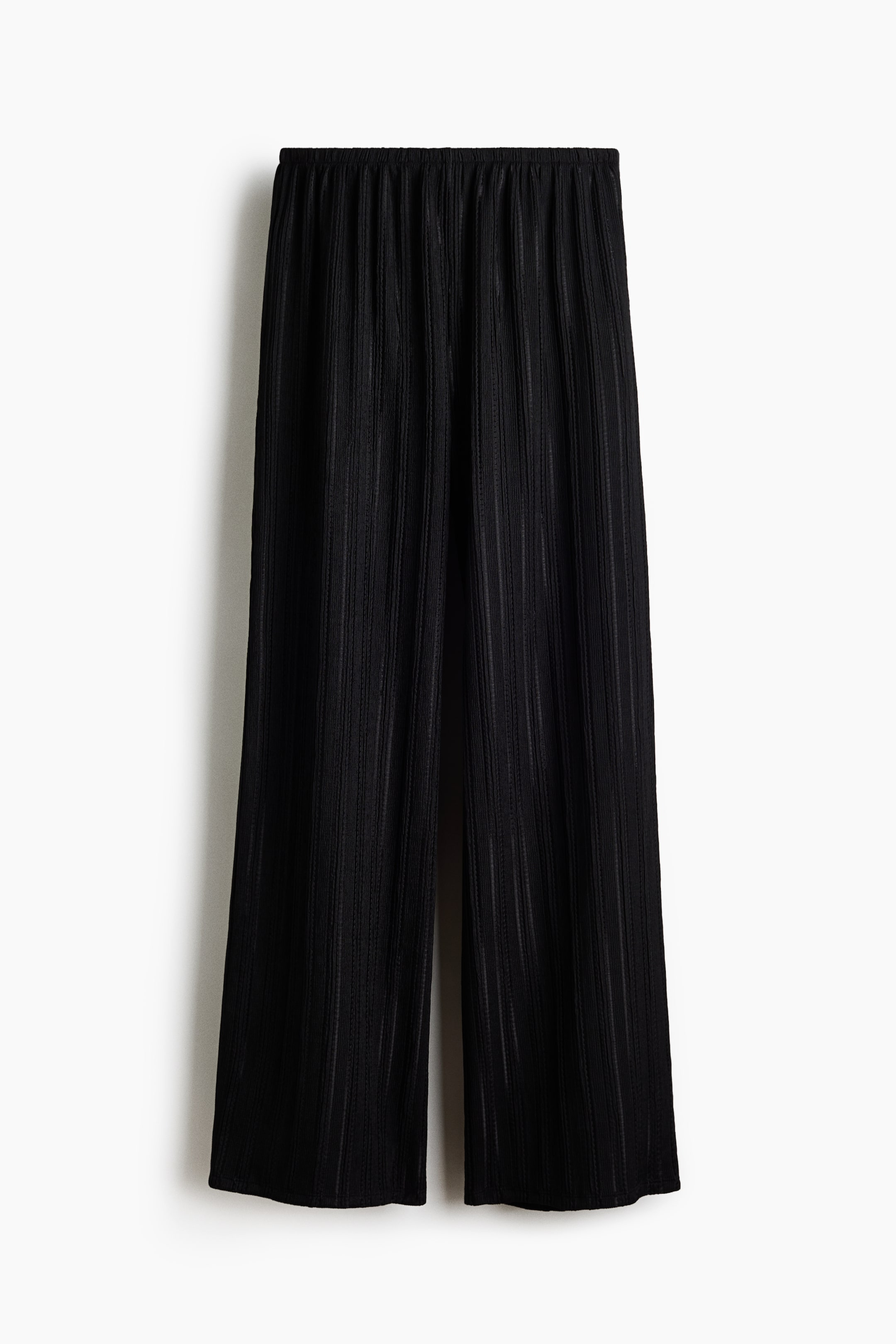 Ampliar la imagen: Pantalones negros de corte holgado presentados desde el frente, mostrando una fina textura de punto calado, una cintura baja elástica y piernas anchas.