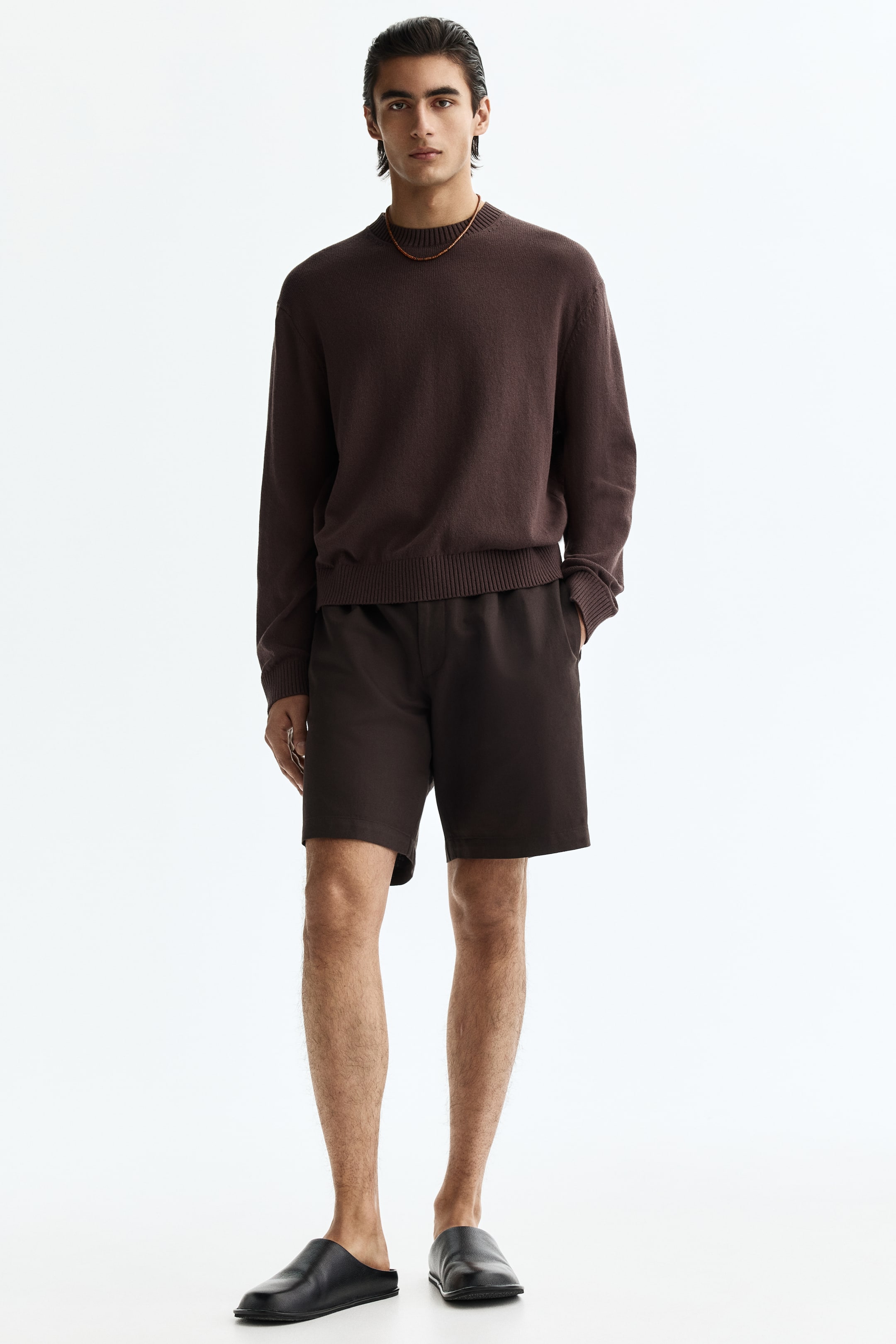 View larger image: "A dark brown crewneck knit sweater, featuring ribbed cuffs and hem, is being worn. It is paired with matching dark brown casual shorts, showing side pockets, and black slip-on mules are completing the ensemble."