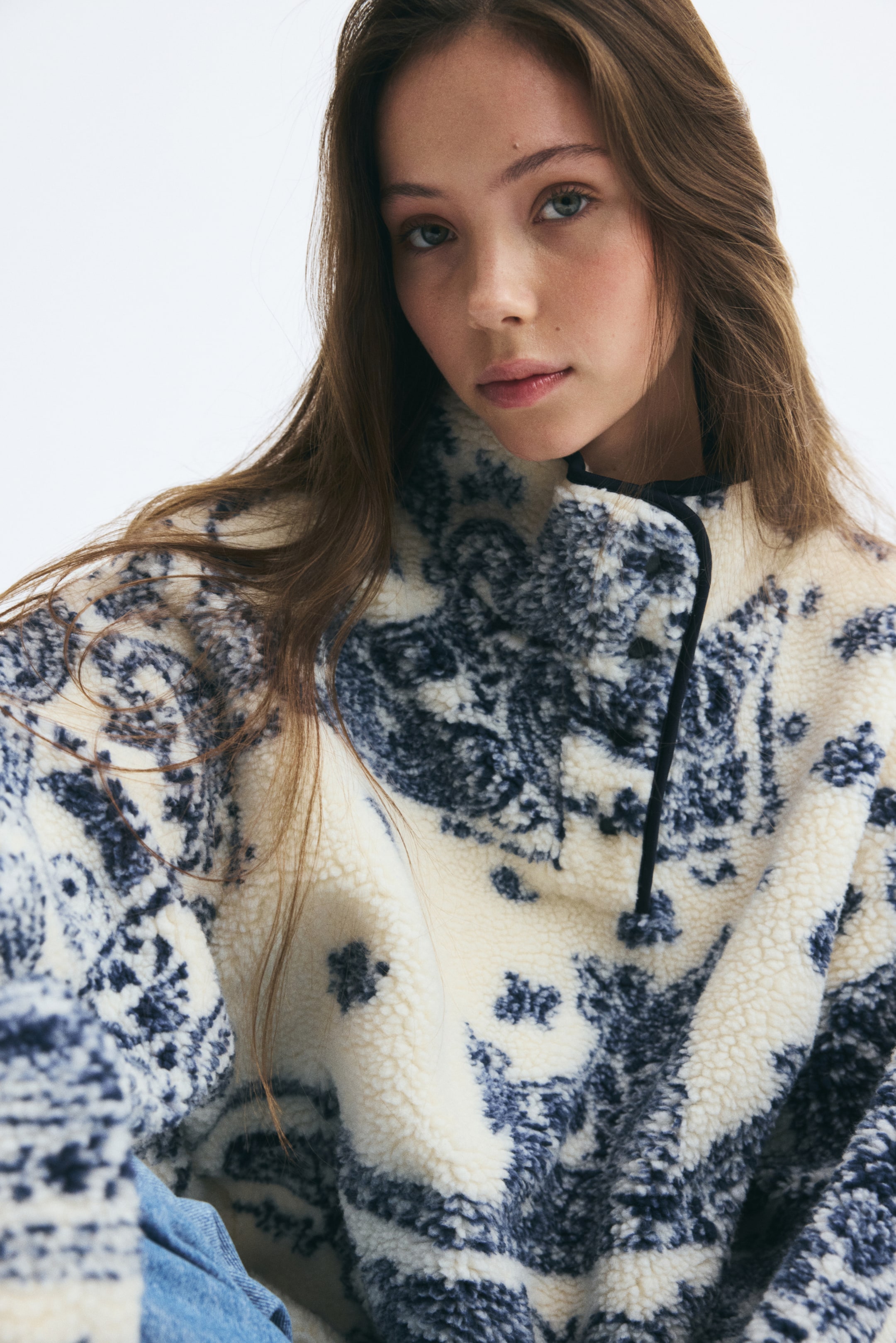View larger image: A soft teddy fleece sweater with a cream and dark blue printed design is being worn by the model. The sweater features a high stand collar with black narrow binding and a buttoned front placket.
