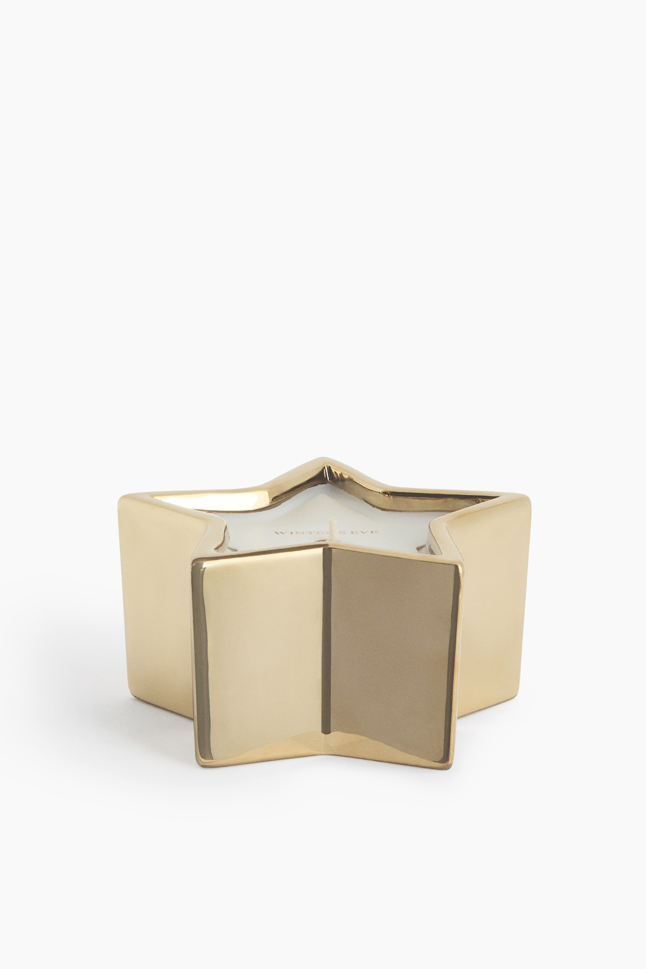 View larger image: A star-shaped candle features a reflective metallic gold container with five points. The white wax inside shows a single central wick and faint gold-coloured text on its surface.