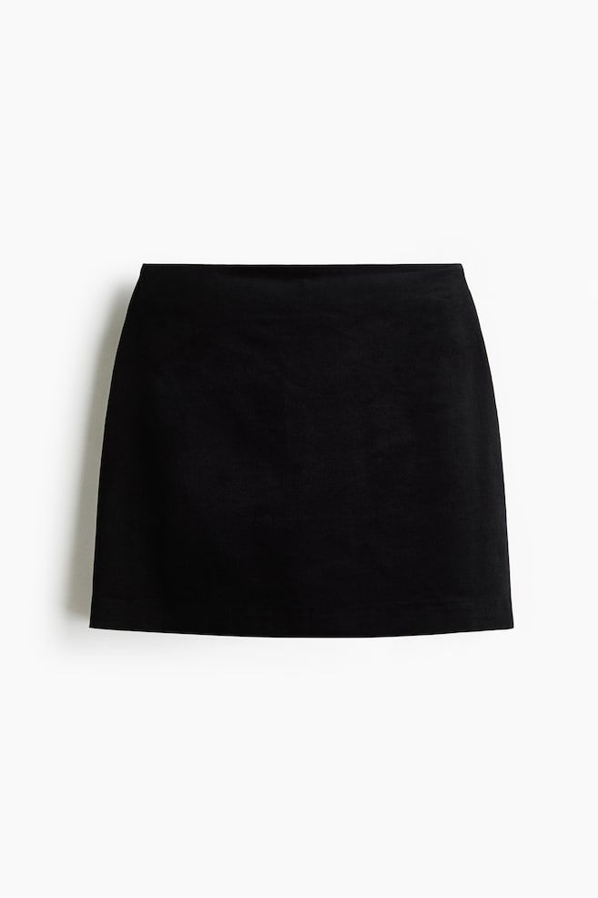En svart minikjol visas framifrÃ¥n och uppvisar en strukturerad, minimalistisk design med en ren, sÃ¶mlÃ¶s linning. Plagget har en diskret A-linjeformad silhuett och en rak fÃ¥ll i matt svart tyg. - 1