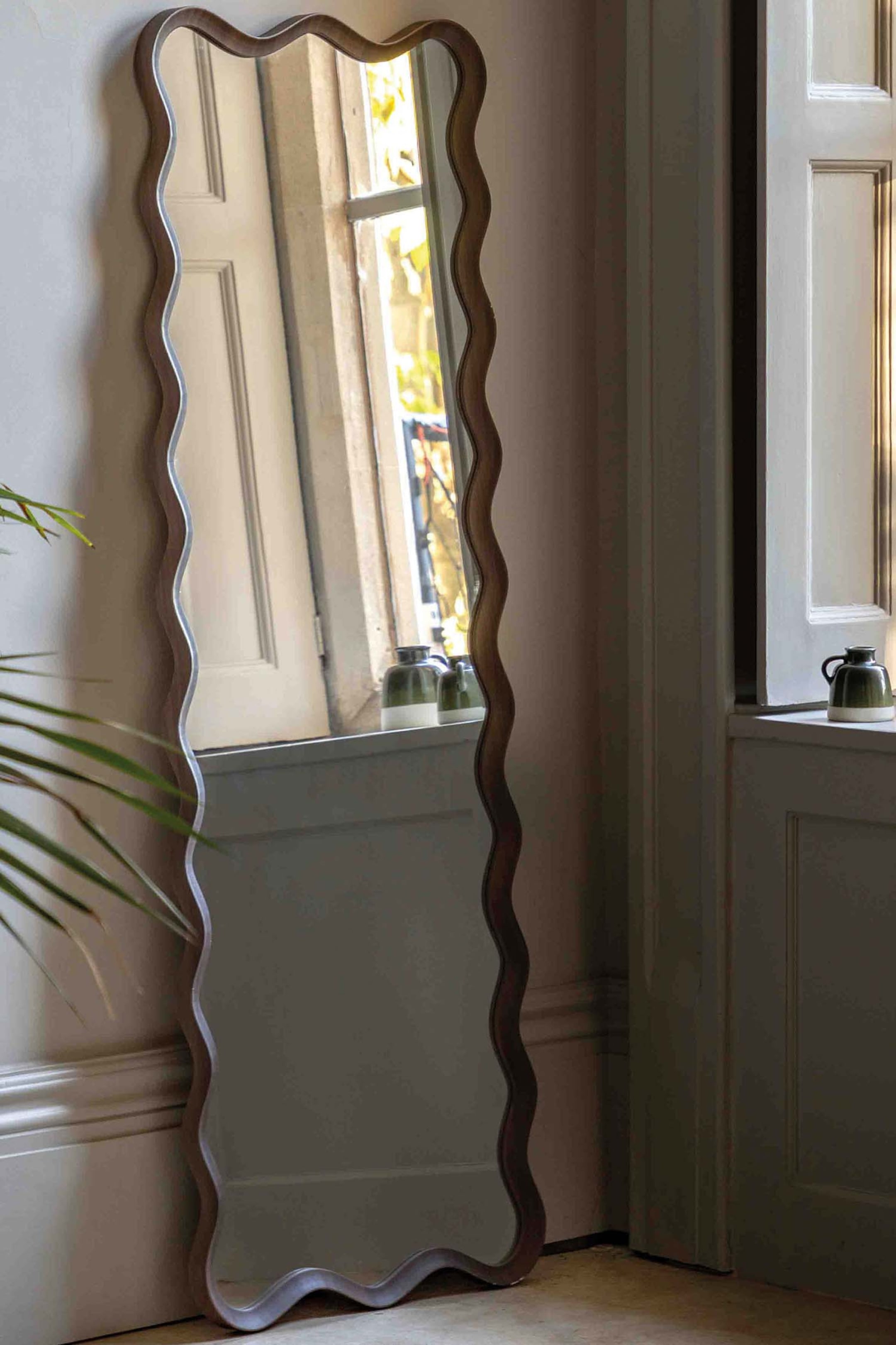 View larger image: A tall, full-length mirror featuring a dark wooden frame with a distinctive wavy edge, standing upright and leaning slightly.