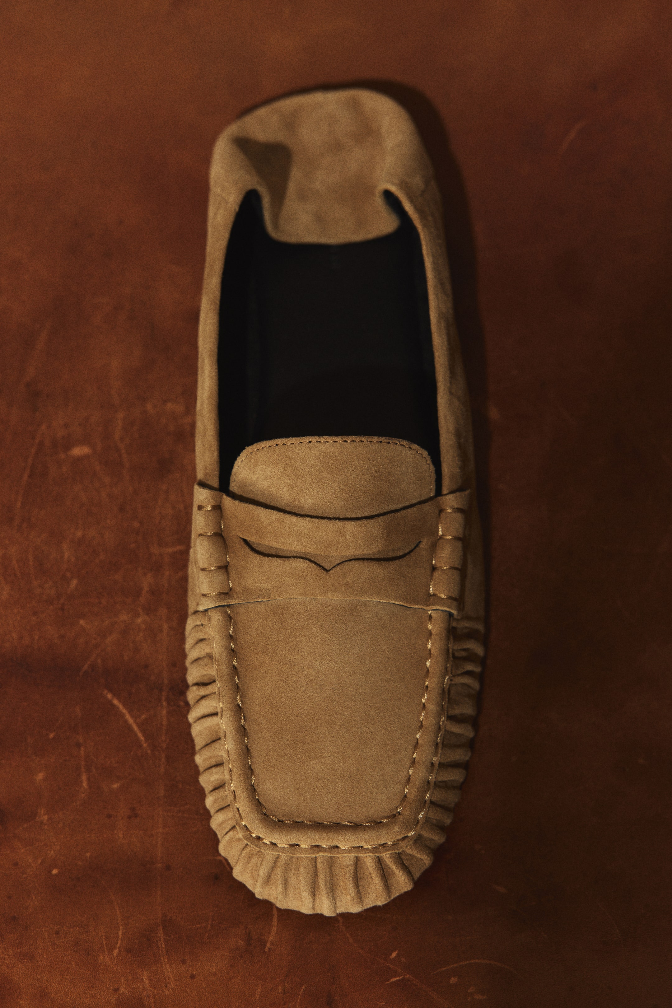 Visualizza immagine più grande: Un loafer in suede color cammello, in stile mocassino, è mostrato in vista dall'alto, rivolto in avanti. Presenta cuciture moc-toe intorno alla punta e la classica fascia penny sulla tomaia.