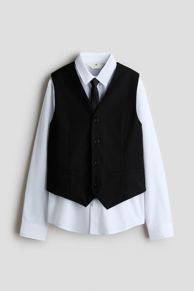 A formal clothing set featuring a black waistcoat, a white long-sleeved shirt, and a black tie is shown from the front. The sleeveless waistcoat is presenting a V-neckline, a four-button front closure, and two front welt pockets, layered over a classic white button-down shirt with a pointed collar and a black necktie. - 1
