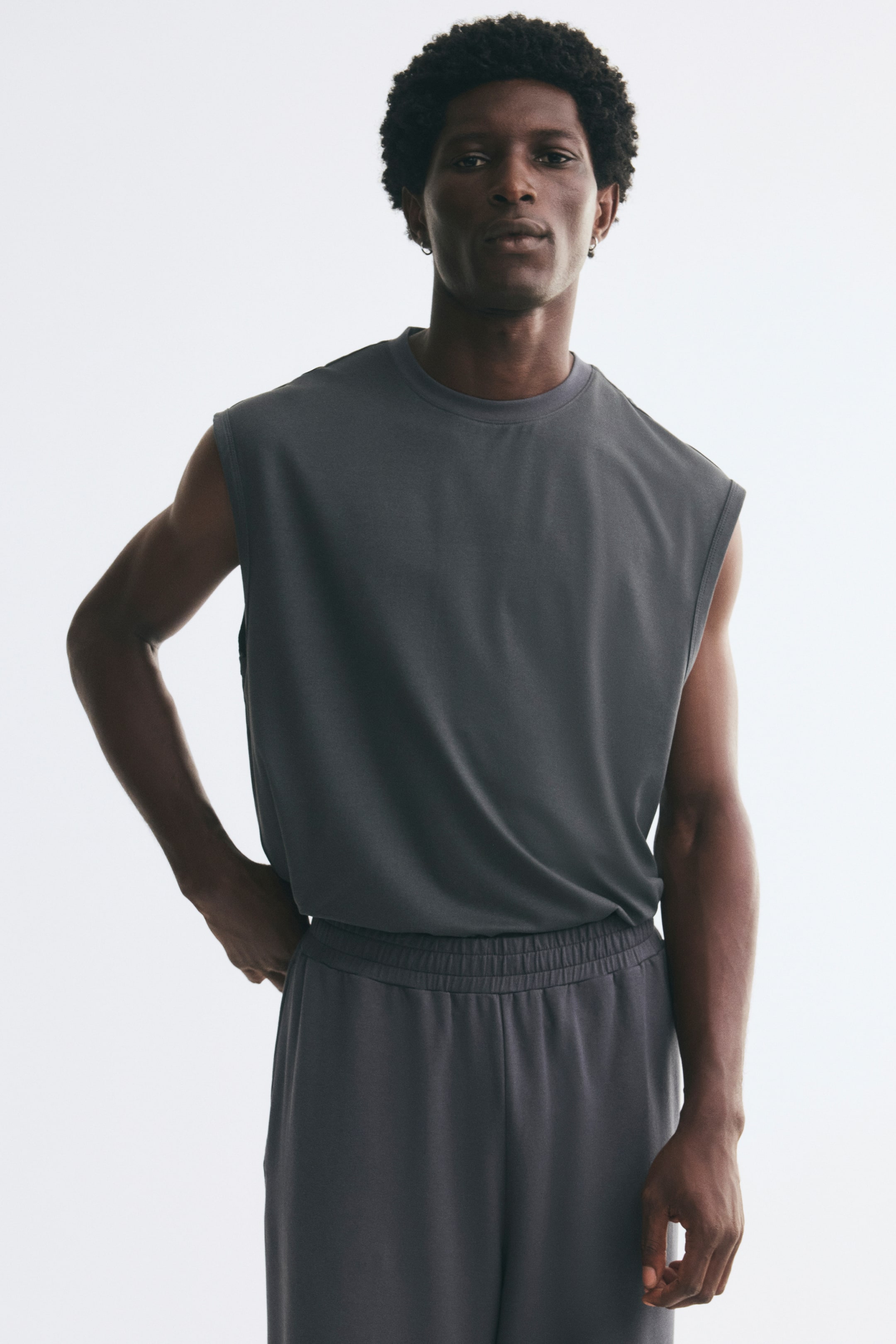 Voir une image plus grande: Un haut camisole en jersey gris foncé, à coupe décontractée, avec un col rond à bord-côte et de profondes emmanchures, est porté par le mannequin. La camisole est rentrée dans un pantalon assorti à taille élastique.