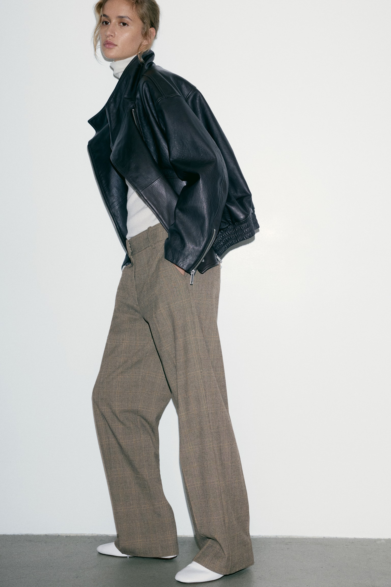 These loose-fit tailored trousers in a brown plaid twill are shown from the front, featuring straight legs with sharp, defined creases running down the centre. The design includes diagonal side pockets, belt loops, and a flat front waistband with a concealed closure. - 1