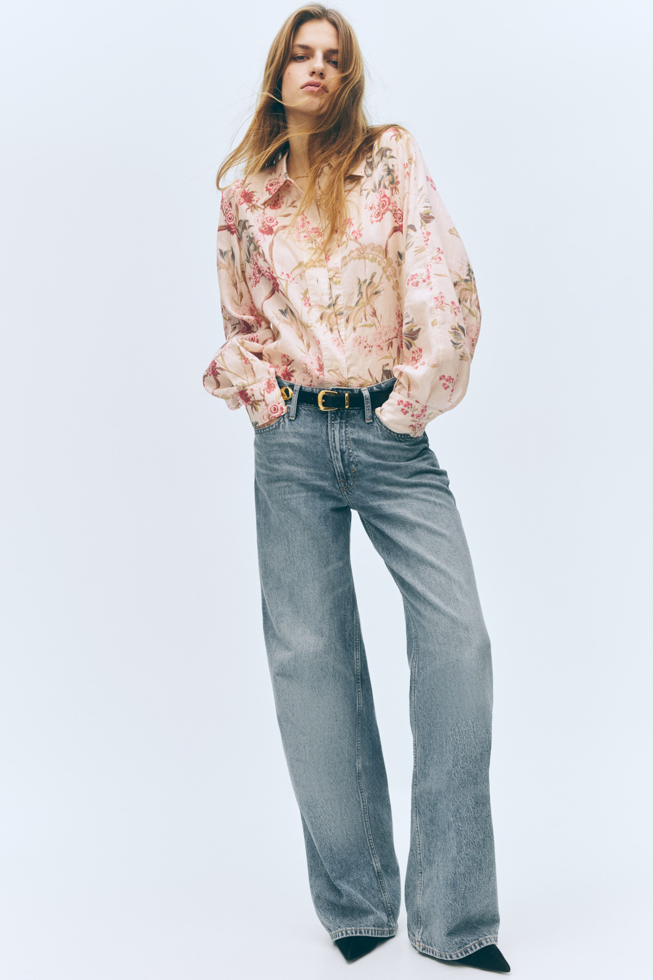 View larger image: A pale pink collared shirt, featuring a pink and green floral print and voluminous sleeves with gathered cuffs, is being presented from a front view. 