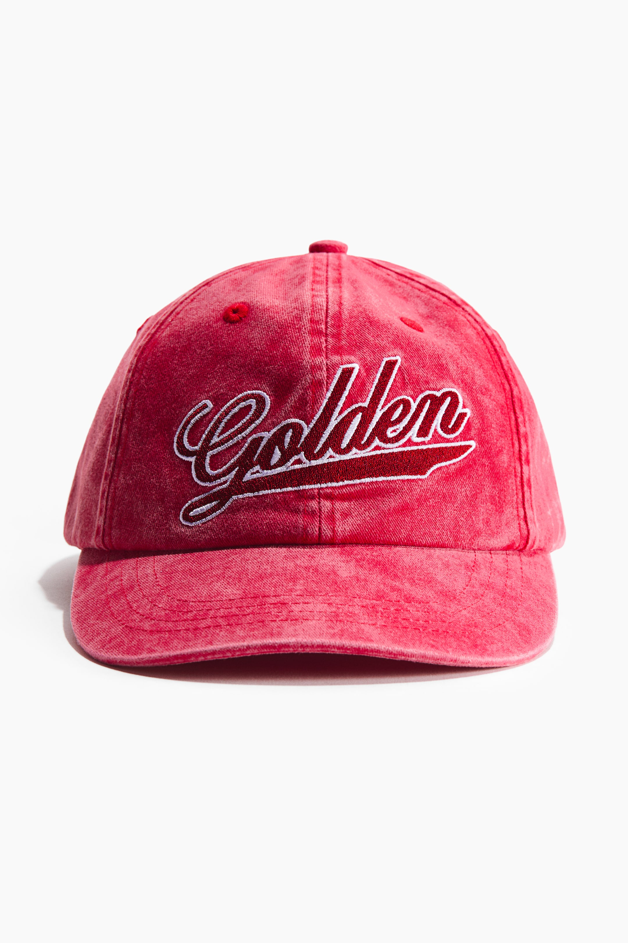 Grösseres Bild ansehen: Eine verblasste rote Baseballkappe zeigt eine abgenutzte Textur, von vorne gesehen. Das Wort "Golden" ist in weißer Schrift mit einem dunkleren roten Umriss und Schatten auf der Vorderseite über einem gebogenen Schirm eingestickt.