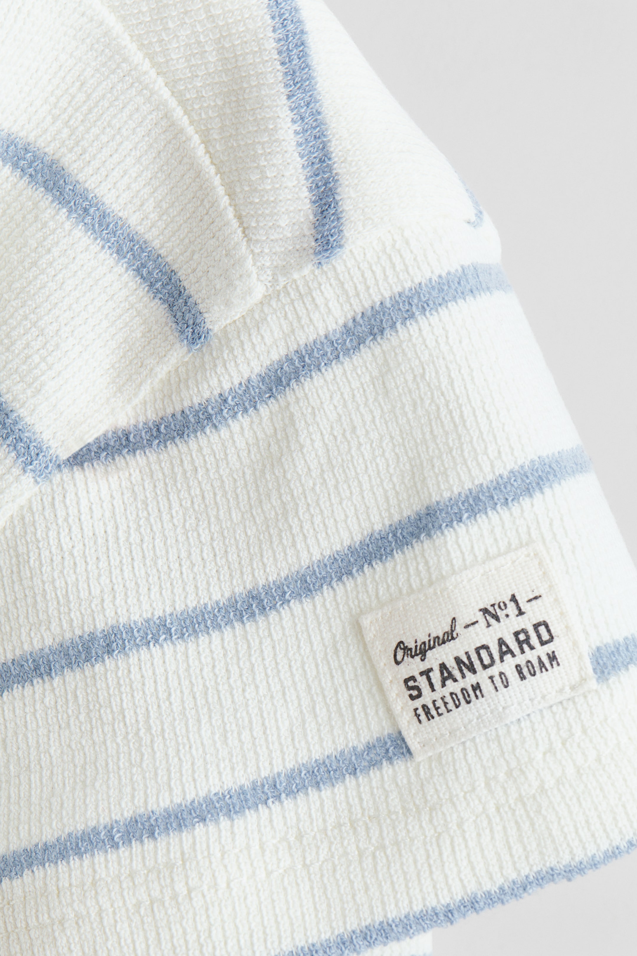 View larger image: The waffle-knit fabric showcases off-white and light blue horizontal stripes. A rectangular fabric label, printed with "Original - N°1 - STANDARD FREEDOM TO ROAM," is stitched onto the fabric.