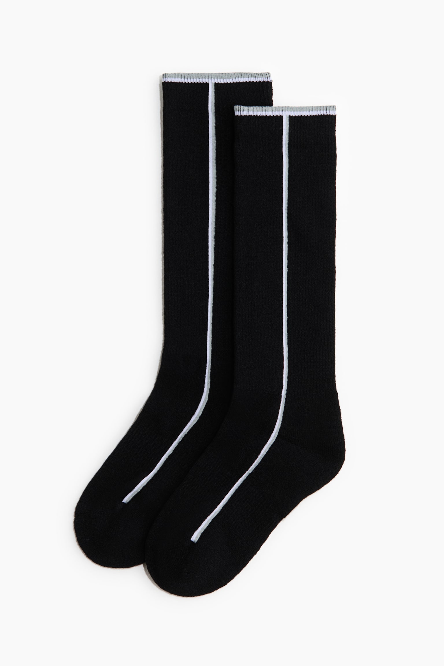 A pair of black crew socks is lying flat, featuring a single vertical white stripe running down the centre front from the cuff to the toe. The socks display ribbed cuffs with a thin, light grey trim at the top edge.