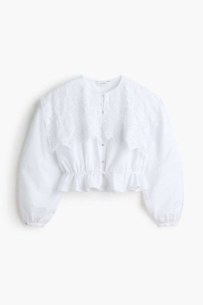 A white cropped blouse is presented facing forward, featuring a large, intricate lace overlay collar, voluminous long sleeves, and a gathered, ruffled hemline with a visible drawstring. - 1