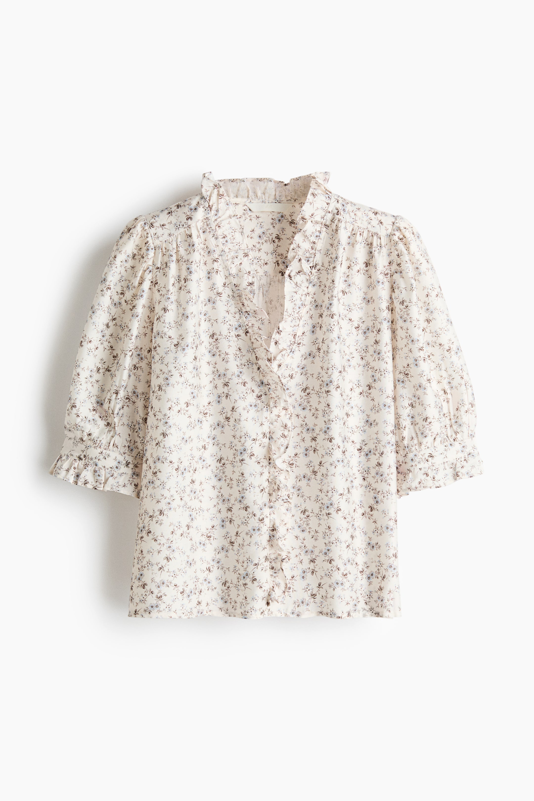 View larger image: An off-white blouse showcases a small, scattered floral print in muted blue and brown tones. It features a ruffled stand-up collar, a V-neckline with ruffles cascading down the button placket, and three-quarter puffed sleeves ending in ruffled cuffs.