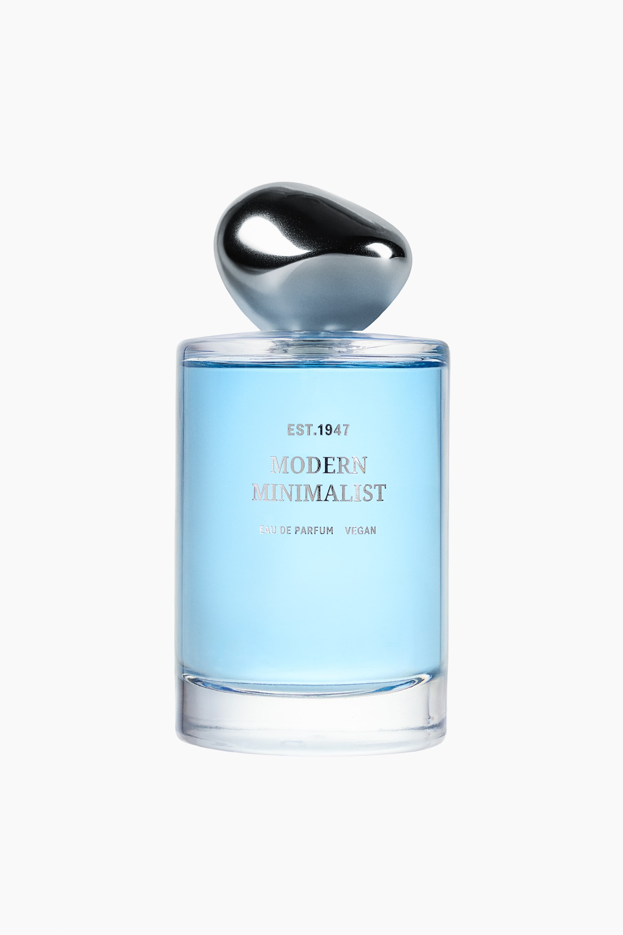 Größeres Bild ansehen: Der Flakon des Modern Minimalist Eau de Parfum steht frontal und präsentiert sein zylindrisches, transparentes Glasdesign, gefüllt mit hellblauer Flüssigkeit. Auf der Vorderseite befindet sich eine minimalistische silberne Beschriftung, und der Flakon ist mit einem polierten, organisch geformten Chromdeckel versehen.