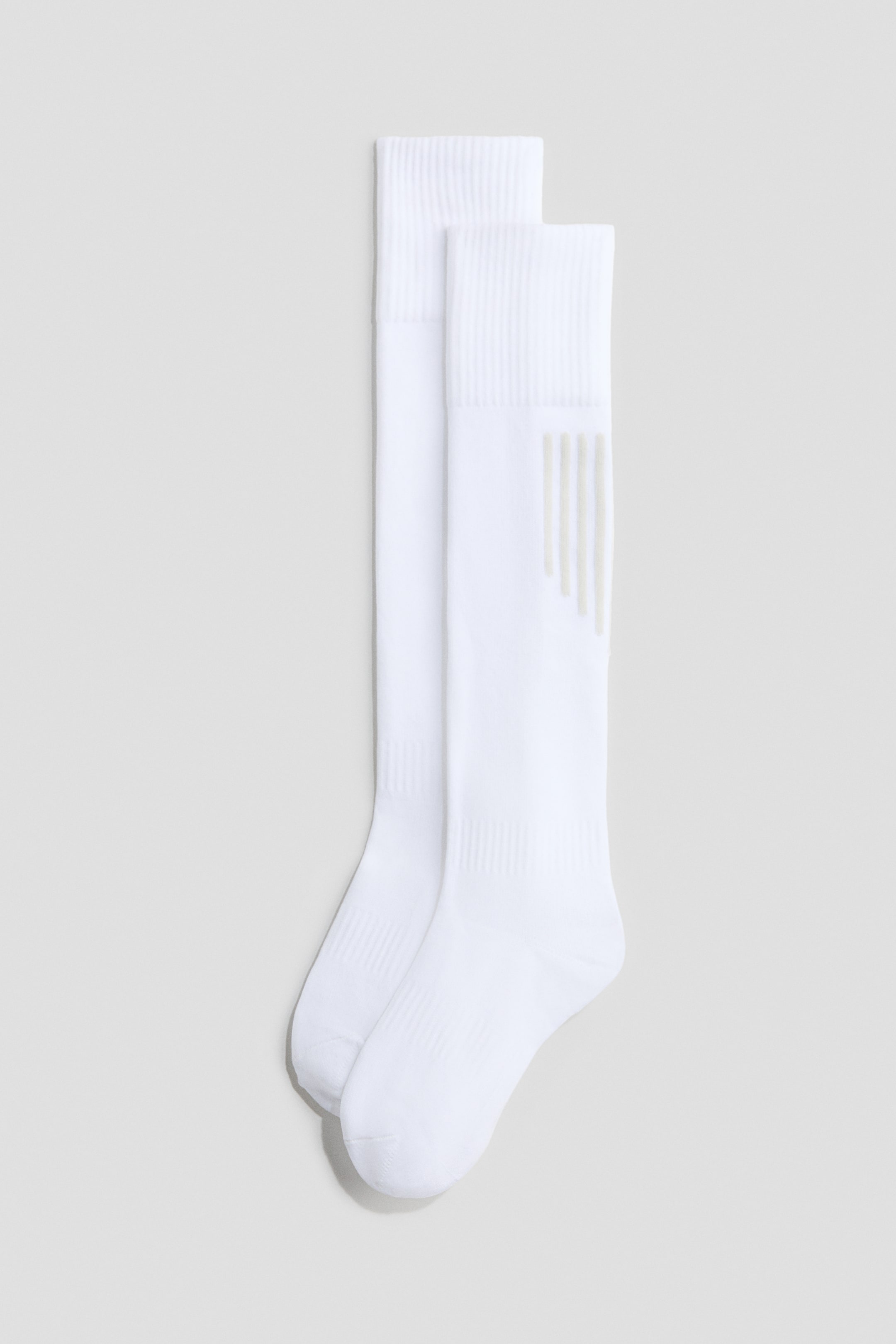 View larger image: Two white knee-length socks are laid flat, slightly overlapping, both adorned with ribbed cuffs. The front sock showcases delicate vertical textured stripes beneath the cuff.