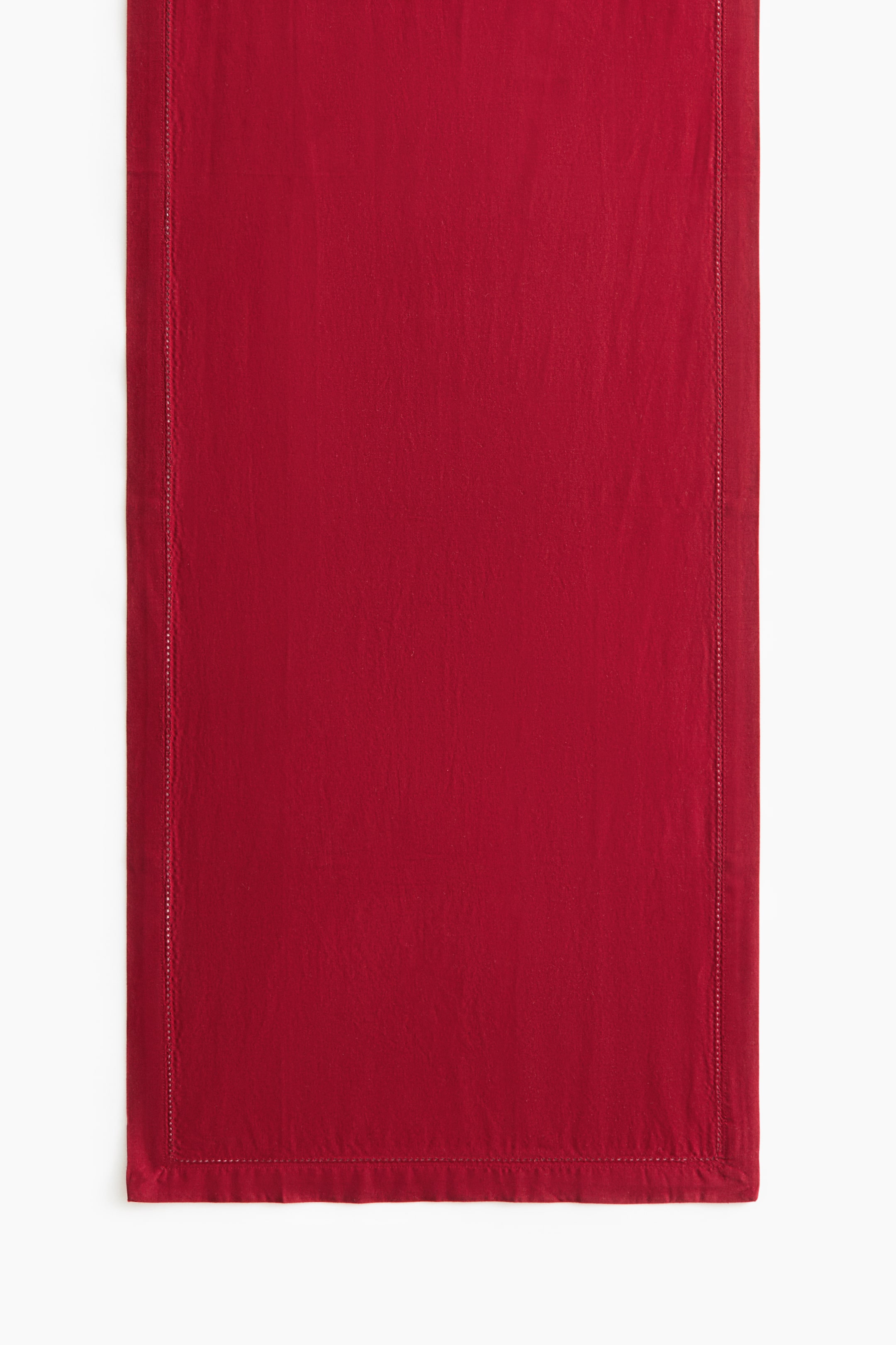 View larger image: A red cotton table runner is shown from the front, showcasing its textured weave and solid colour. The runner features a delicate hemstitching border running parallel to its edges and is finished with a wide folded hem.