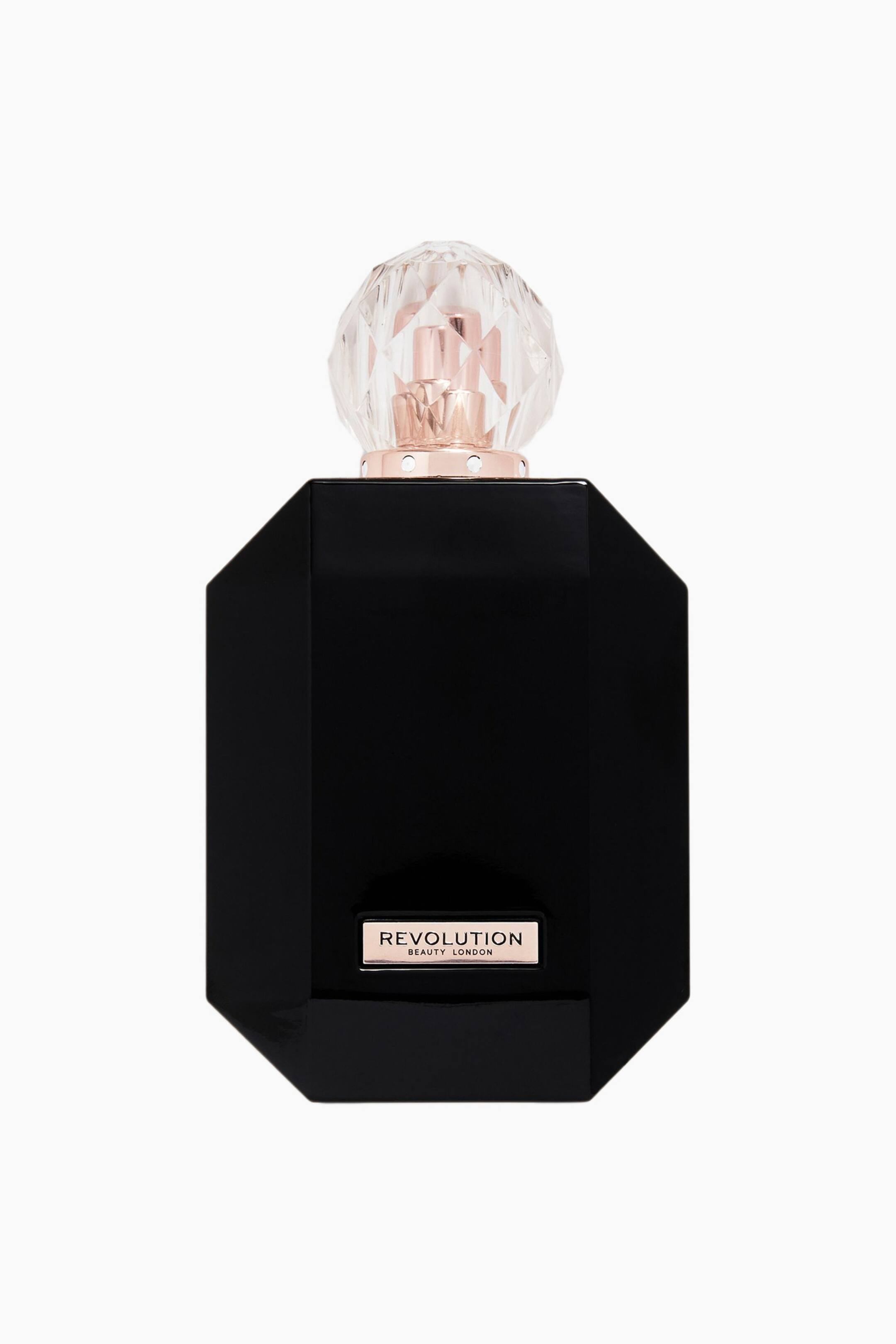 Größeres Bild ansehen: Eine frontale Ansicht einer Parfümflasche mit einem glänzenden, schwarzen, achteckigen Körper. Sie ist mit einer transparenten, kugelförmigen Kappe mit diamantartigen Facetten versehen, die auf einem roségoldenen Kragen sitzt, sowie mit einer kleinen rechteckigen roségoldenen Plakette nahe der Basis, auf der „REVOLUTION BEAUTY LONDON“ zu sehen ist.