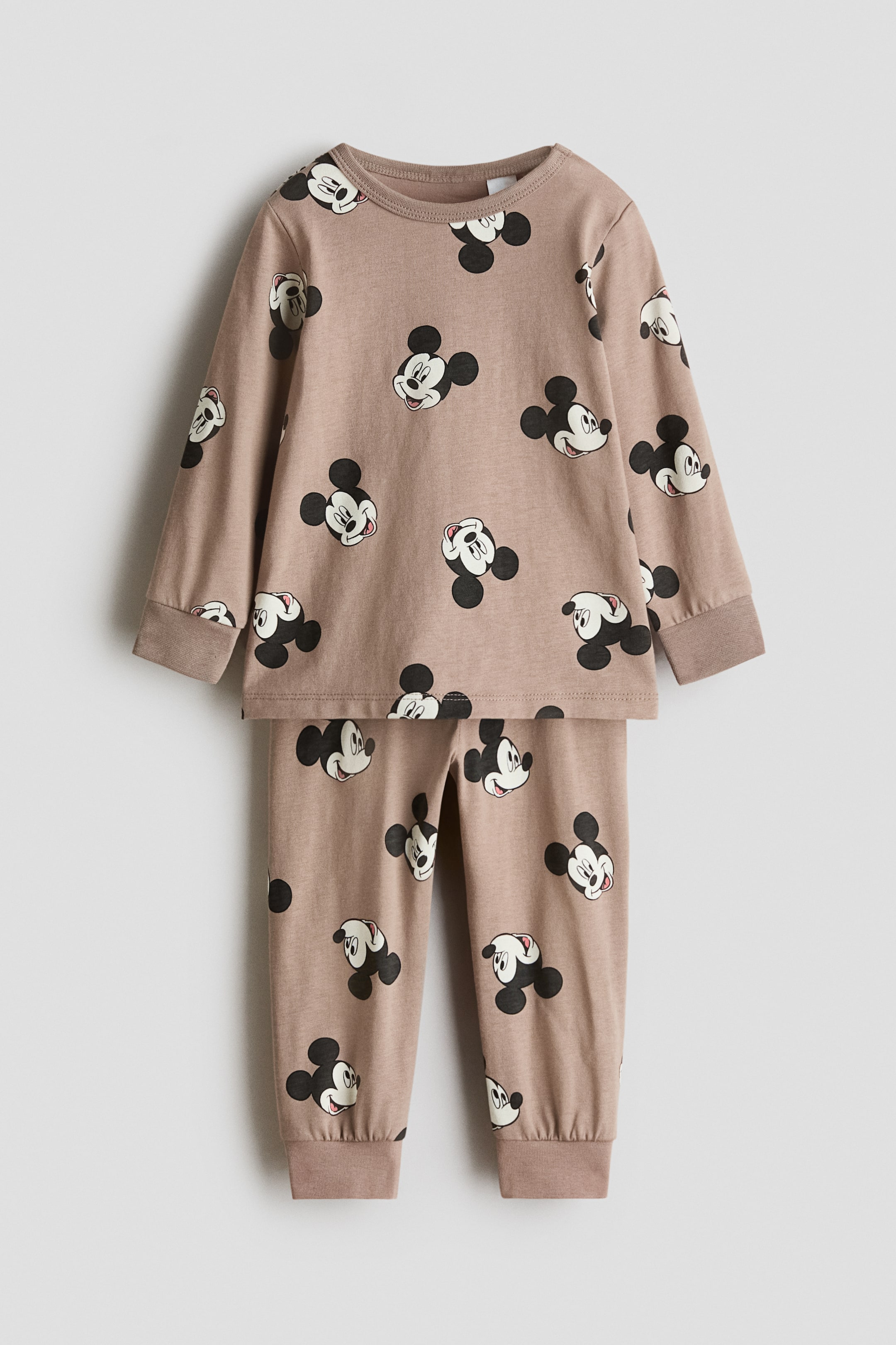 Ver imagem maior: Um conjunto de pijama infantil apresenta uma camisola de manga comprida e calças compridas a condizer em castanho claro, exibindo um padrão repetido de rostos do Mickey Mouse. A camisola é desenhada com uma gola redonda e punhos canelados, e as calças apresentam punhos canelados nos tornozelos.