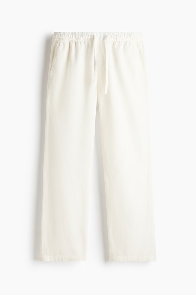 These off-white trousers are shown from the front, featuring a relaxed, straight-leg silhouette with an elasticated waistband and a hanging drawstring. The trousers are displaying side seam pockets and a lightweight, textured fabric. - 1