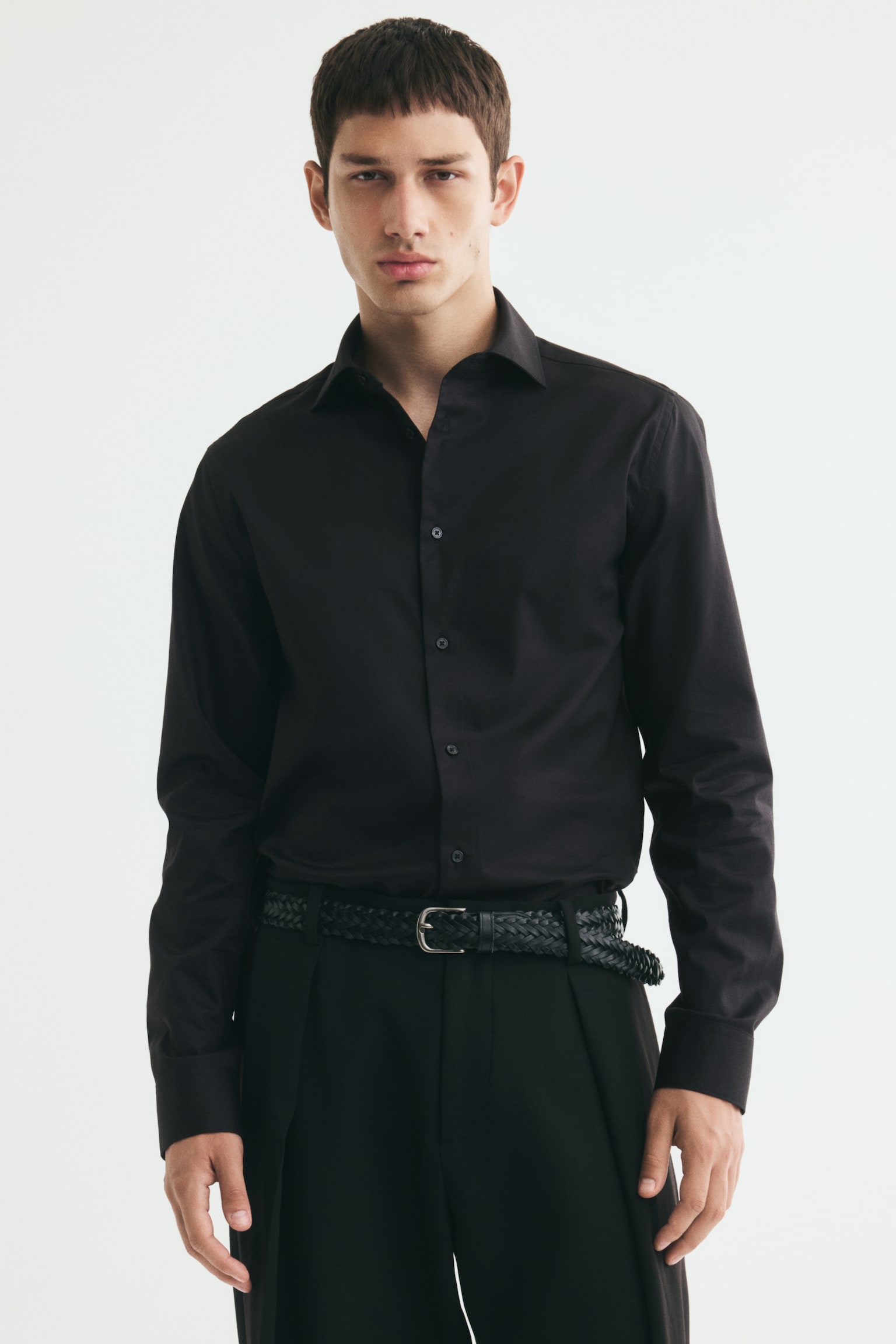 Má»t chiáº¿c Ã¡o sÆ¡ mi cotton Ã´m dÃ¡ng mÃ u Äen, cÃ³ cá» cut-away vÃ  tay dÃ i, Äang ÄÆ°á»£c ngÆ°á»i máº«u máº·c. Ão ÄÆ°á»£c sÆ¡ vin vÃ o quáº§n tÃ¢y Äen, káº¿t há»£p vá»i tháº¯t lÆ°ng Äen kiá»u bá»n. - 1