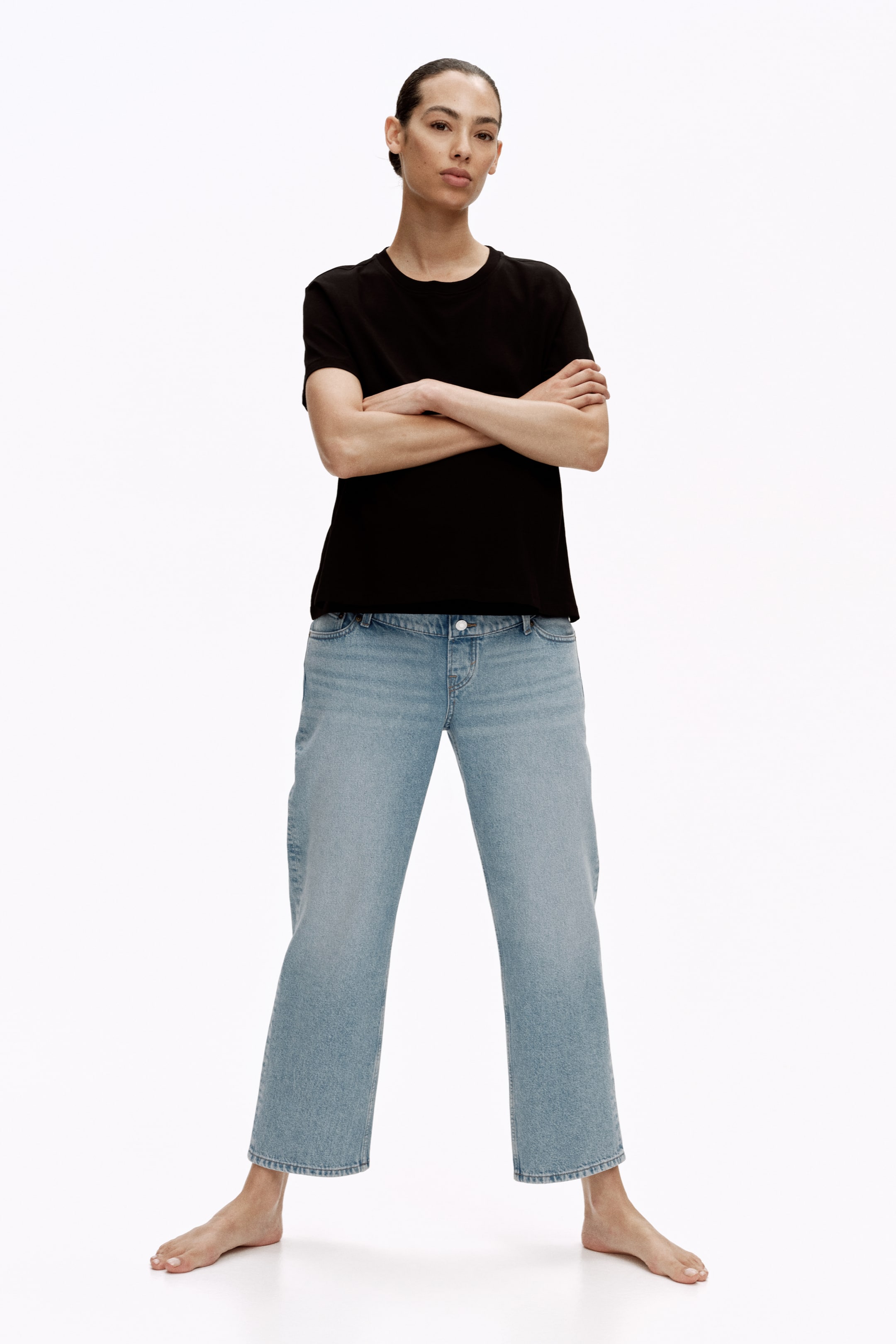 View larger image: The model is wearing light blue, straight-leg 5-pocket jeans. These jeans feature a visible button closure at the waist and hit right at the ankle bone.