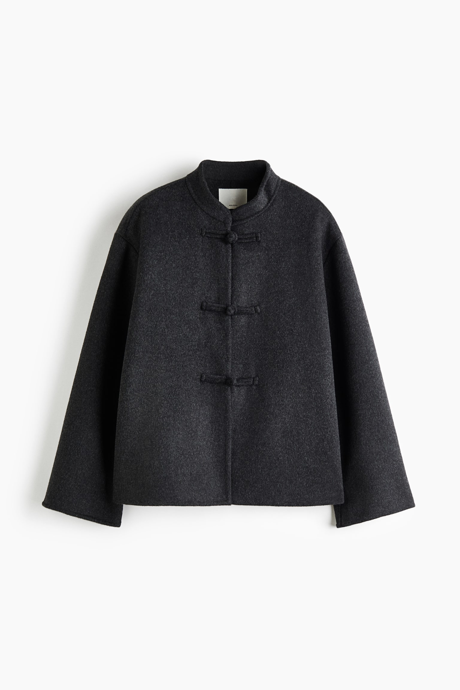 Se muestra de frente una chaqueta oversize de mezcla de lana en color gris oscuro, que destaca por su acabado texturizado y cepillado, asÃ­ como por una silueta cuadrada. El diseÃ±o presenta cuello mao, hombros caÃ­dos con mangas anchas y tres cierres frontales con botones de nudo de tela. - 1
