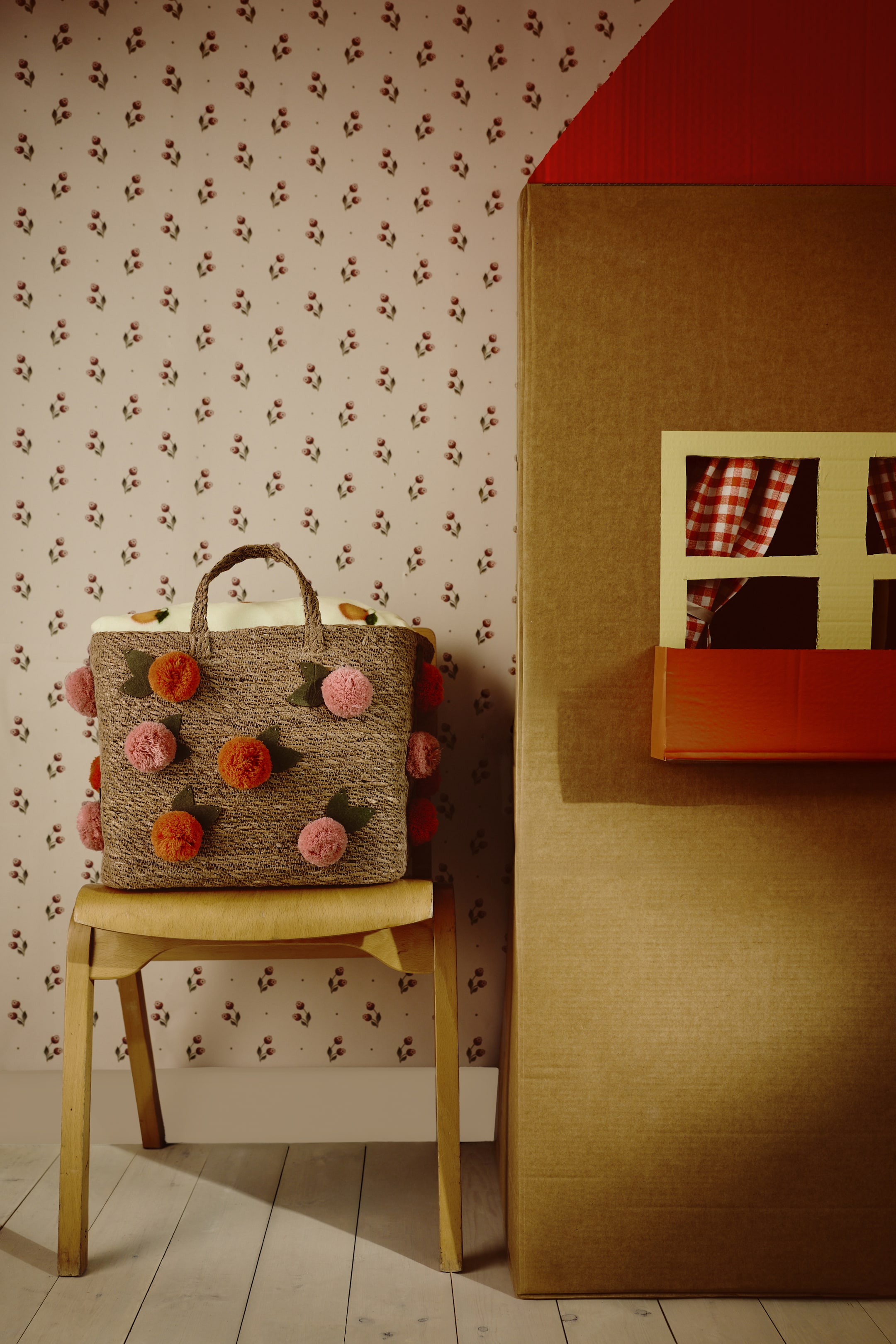 Nagyobb kép megtekintése: "Elöl tűnik fel egy tároló kosár, amely fonott tengeri fűből készült. A tetején két fonott fogantyú található, és játékos rózsaszín és narancssárga pomponokkal van díszítve, amelyeket kis zöld filc levelek kísérnek."