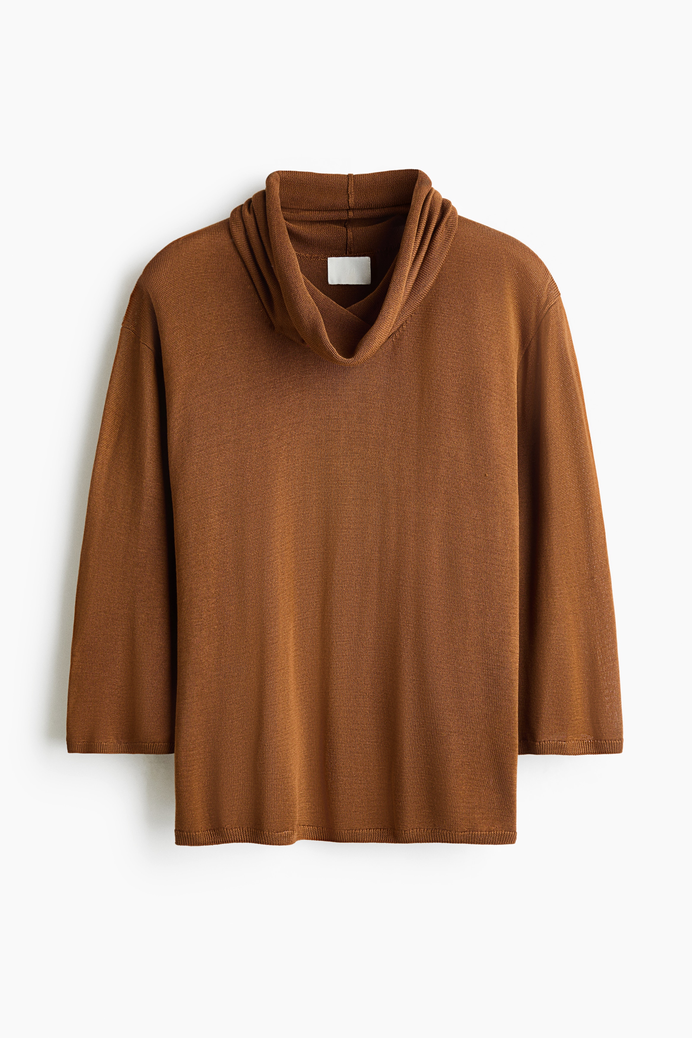 A brown knitted top featuring a draped cowl neck, dropped shoulders, and three-quarter-length sleeves with ribbed cuffs is being worn by the model. The top is styled with light-coloured jeans.