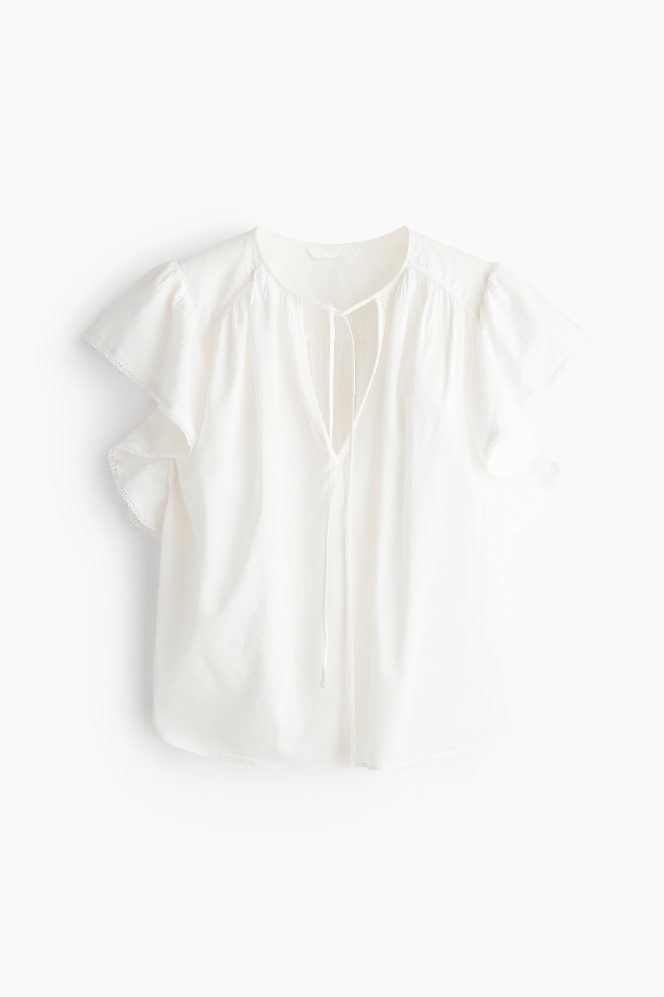 View larger image: An oversized white blouse is displayed from the front, showcasing an airy weave, a round neckline with narrow ties forming a V-shaped opening, voluminous flutter sleeves with delicate lace trim at the cuffs, and gathered detailing at the shoulders.