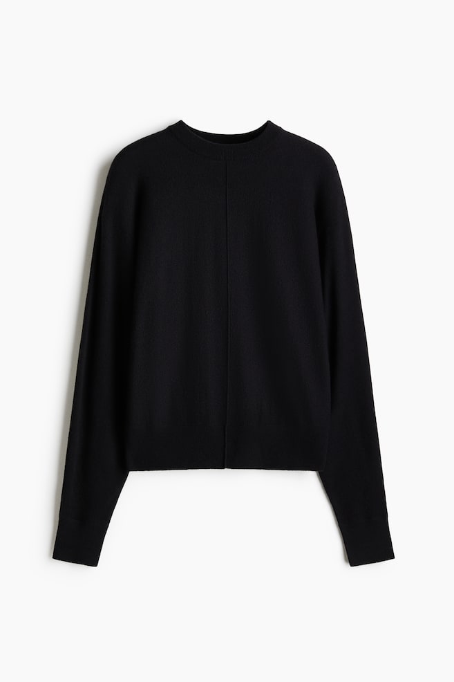 A black finely knitted sweater is laid flat, facing forward, showcasing a crew neck and long sleeves with ribbed cuffs. A vertical seam runs down its center front, and a ribbed hem is visible at the bottom. - 1