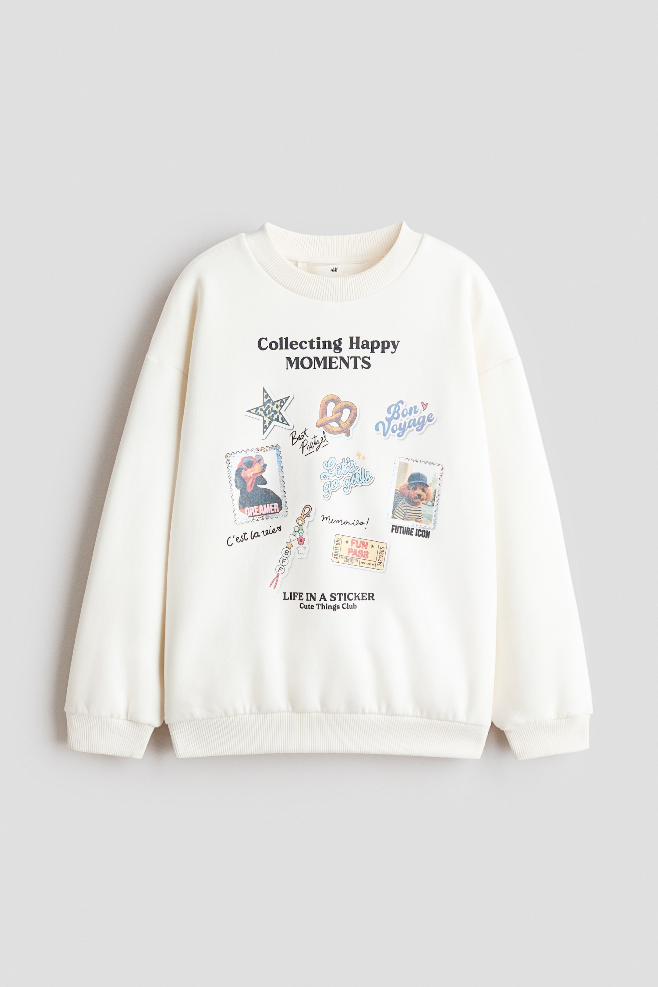 View larger image: A loose-fit, off-white sweatshirt is facing front, featuring a round, rib-trimmed neckline, dropped shoulders, and long sleeves with ribbed cuffs and hem. The front is displaying a colourful printed design with the text "Collecting Happy MOMENTS" surrounded by various sticker-style graphics, including dog portraits, a star, and a pretzel.