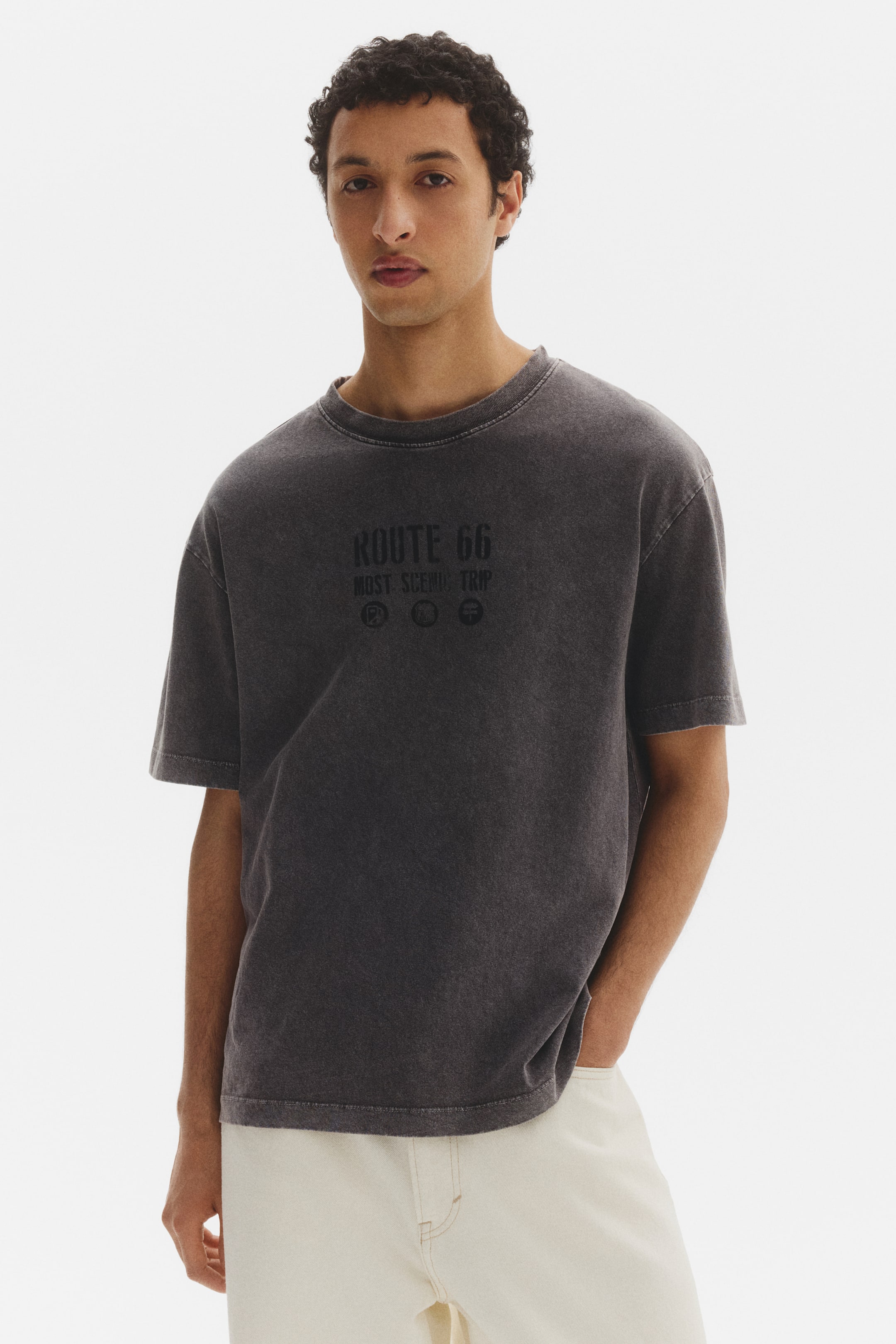 View larger image: A deep grey, stone-washed t-shirt featuring a crew neck, short sleeves, and a dark graphic on the front. The graphic displays "ROUTE 66," "MOST SCENIC TRIP," and three small circular icons.
