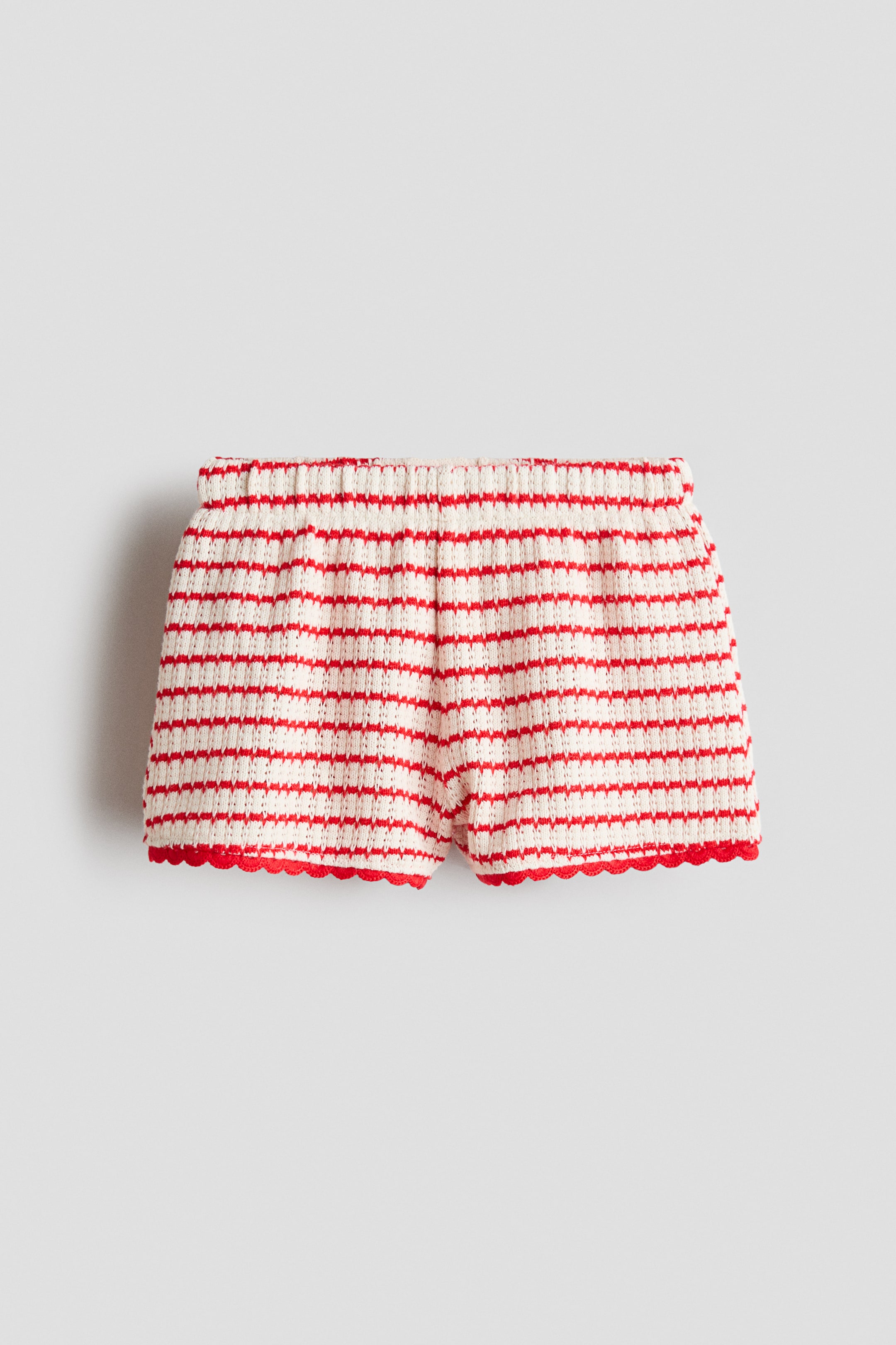 Ver imagen más grande: Los pantalones cortos se presentan desde el frente, mostrando un suave tejido de punto con franjas horizontales alternas en rojo y crema. Una cintura elástica recoge la parte superior de los pantalones cortos, y las aberturas de las piernas presentan dobladillos ondulados en rojo.